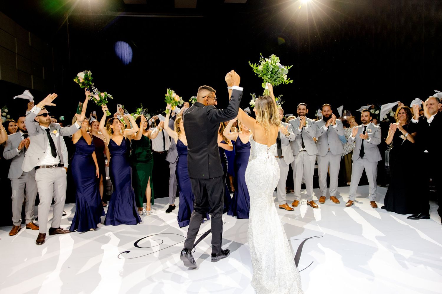Wedding party and guests cheer during reception celebration on white dance floor.