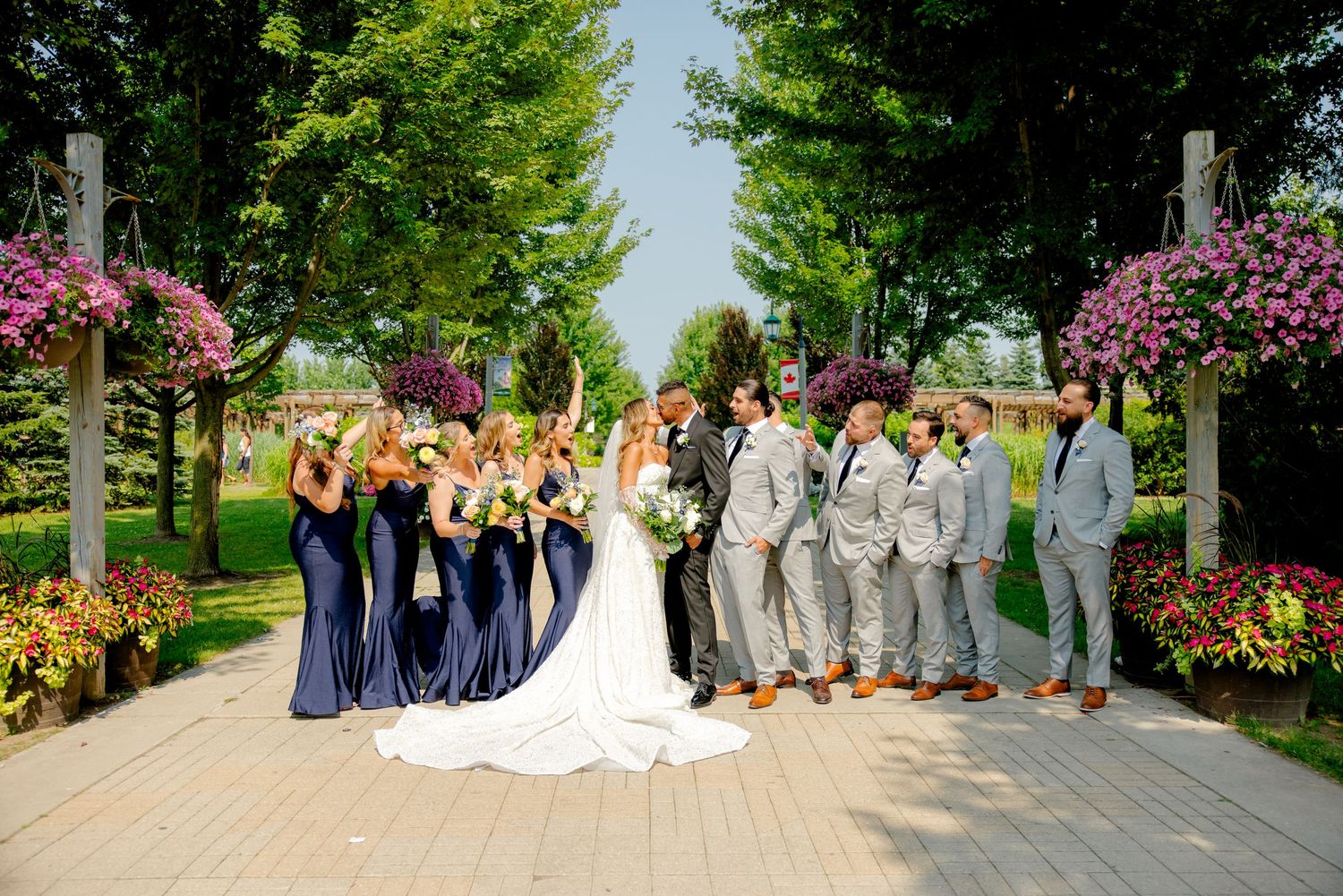 Large wedding party poses on stone pathway with vibrant flower arrangements.