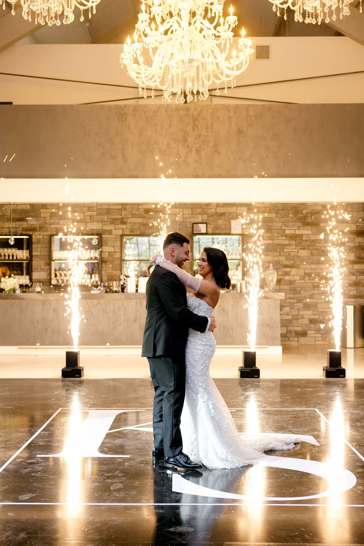 Couple shares romantic moment on illuminated dance floor with elegant chandelier overhead.