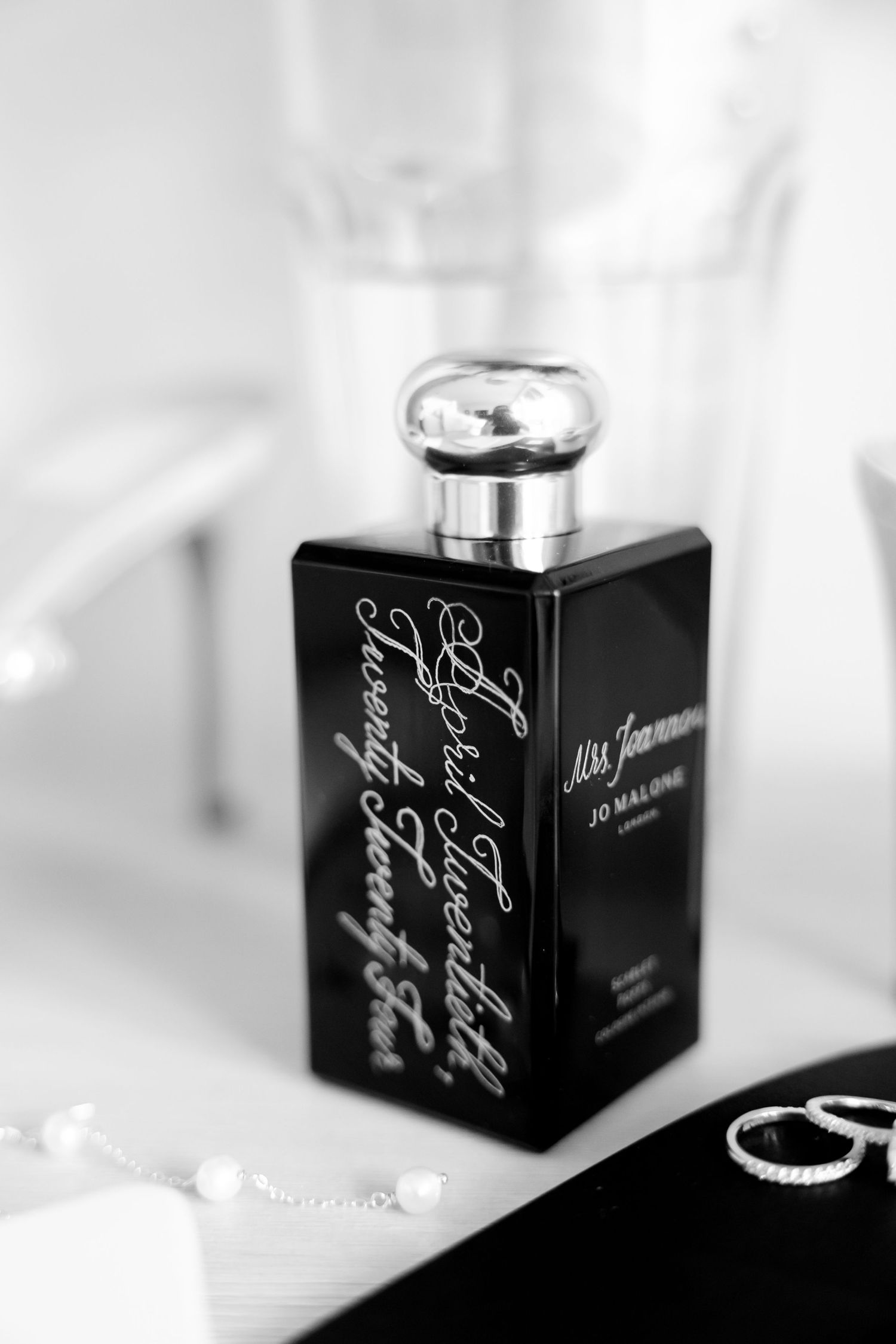 Black perfume bottle with silver cap and elegant cursive text displayed in monochrome.