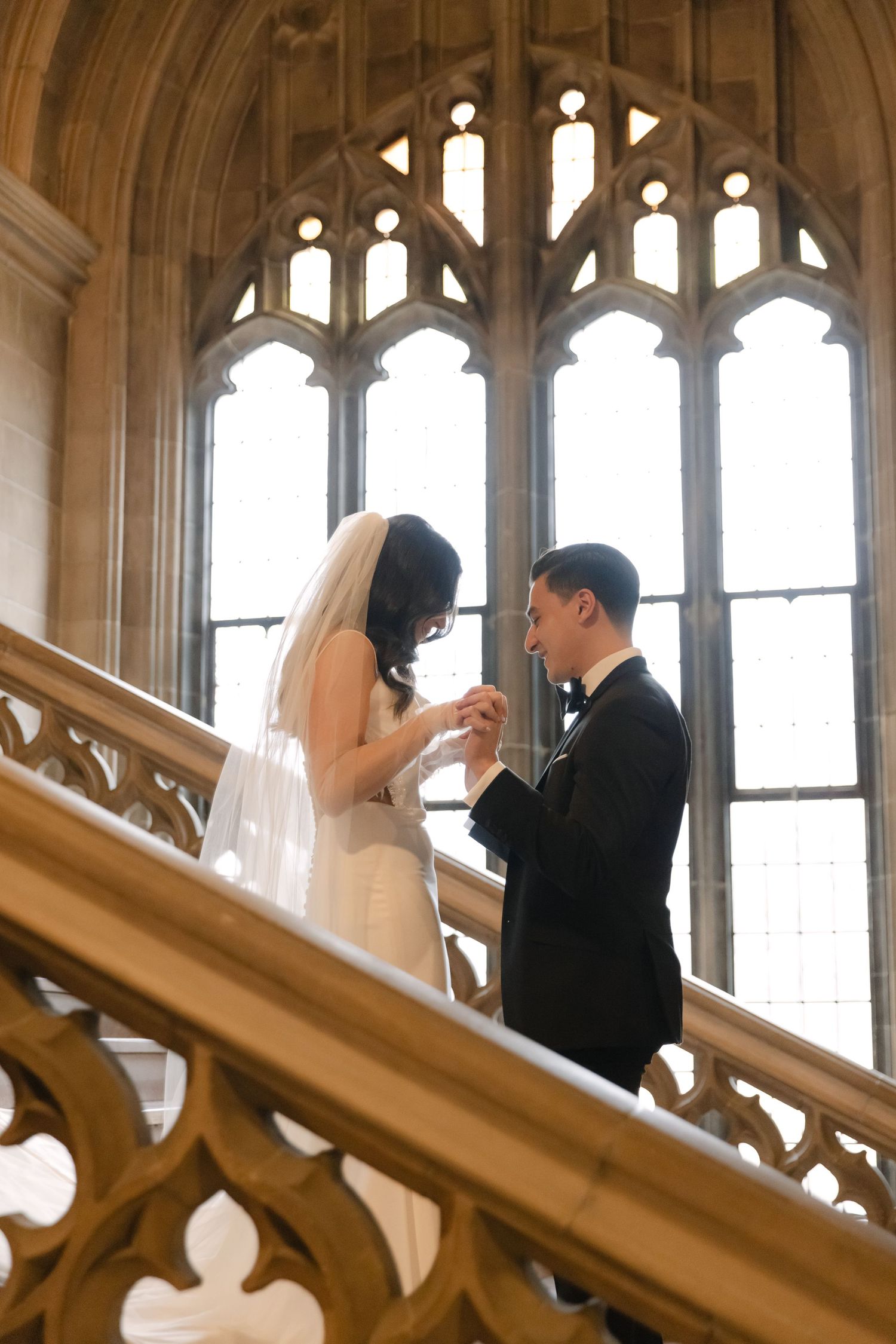 A tender wedding moment on a grand staircase with ornate gothic windows in the background.