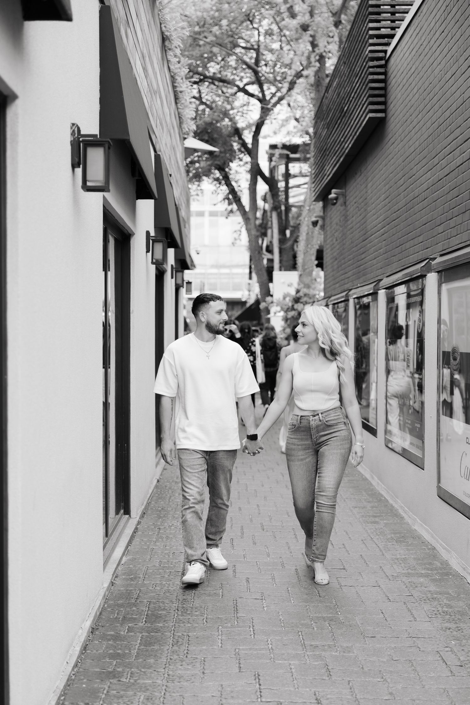 A couple holding hands while walking down a brick-paved street in black and white photography.