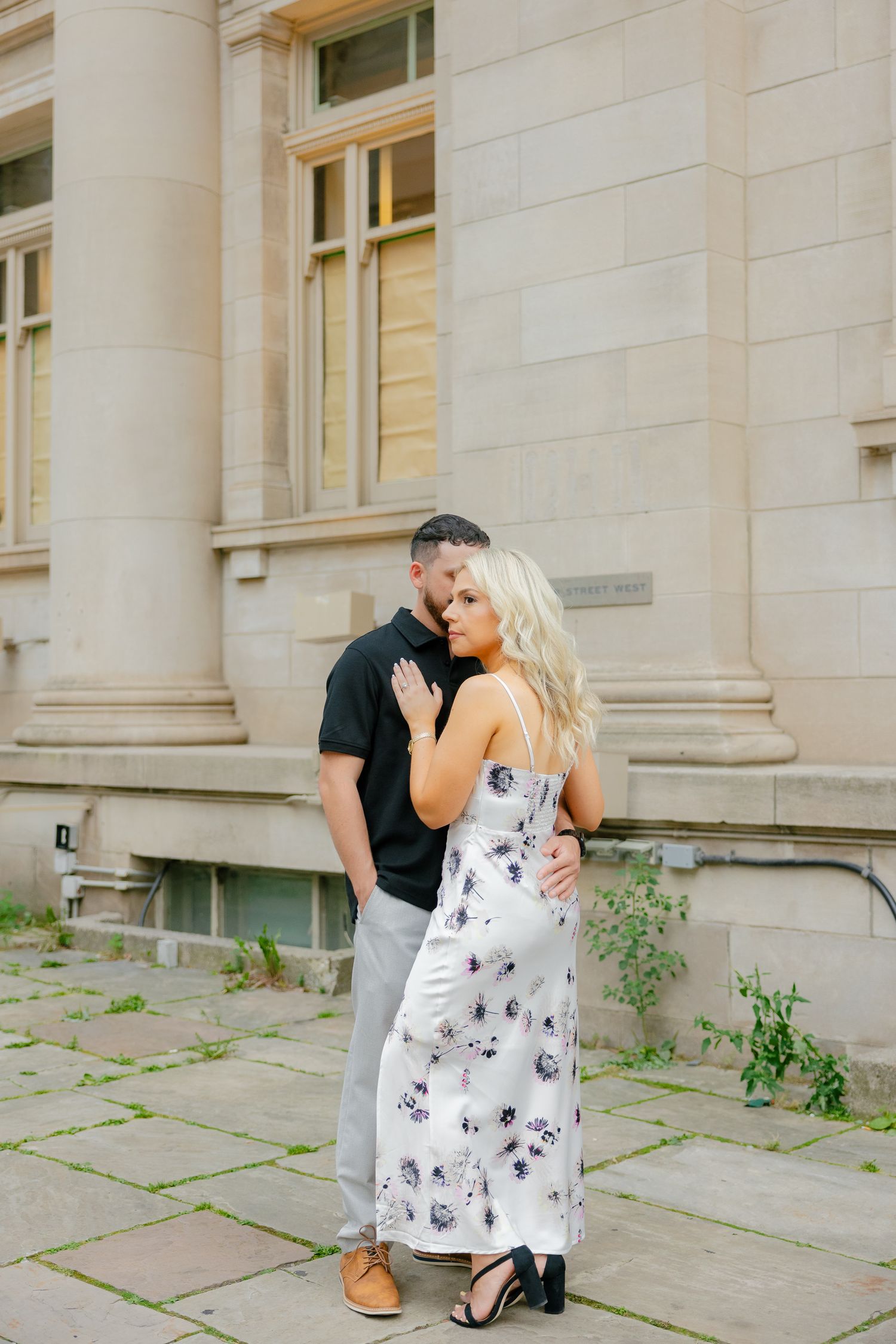 Couple sharing intimate moment against limestone building backdrop.