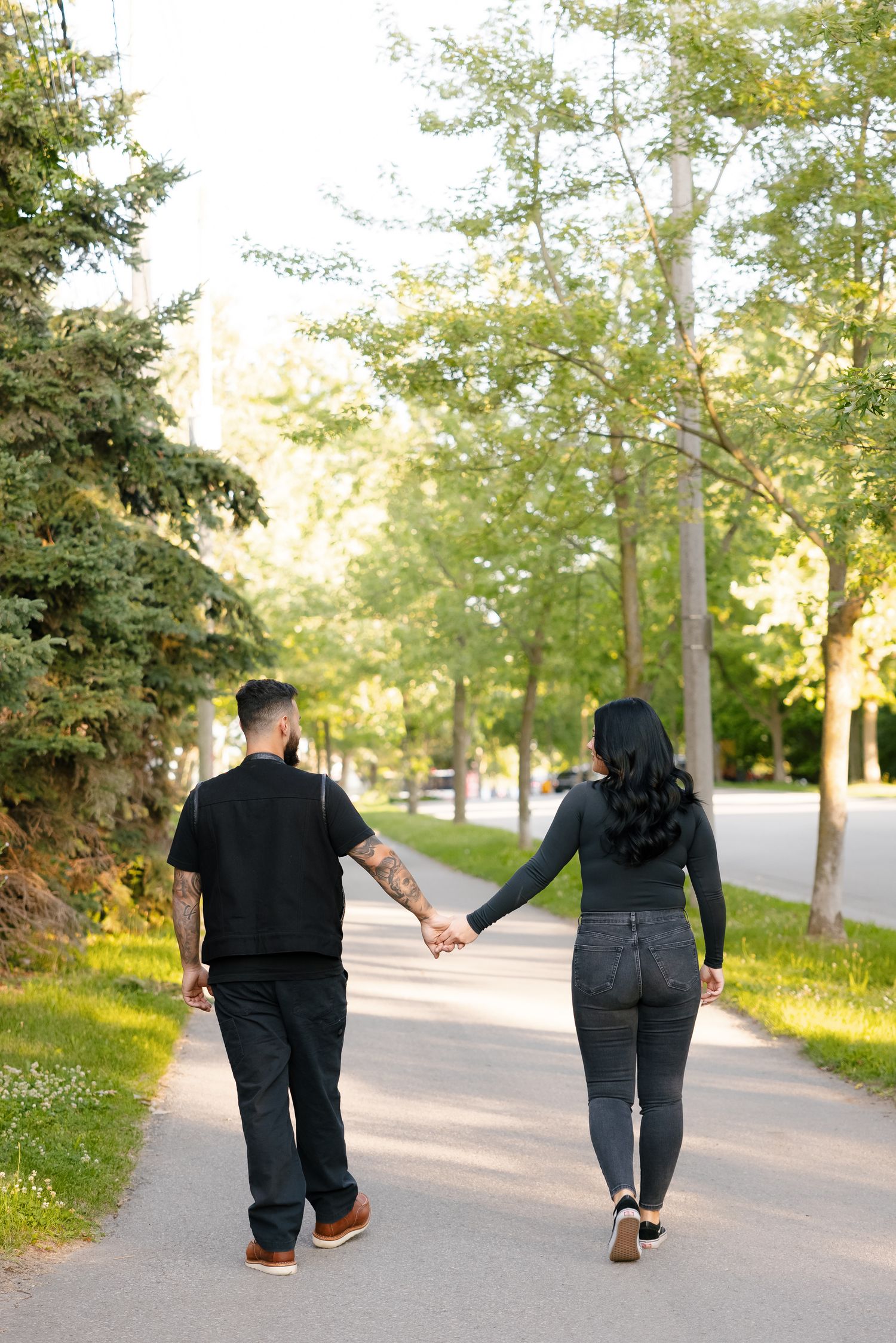 A couple walking hand in hand on a tree-lined path during a sunny afternoon.