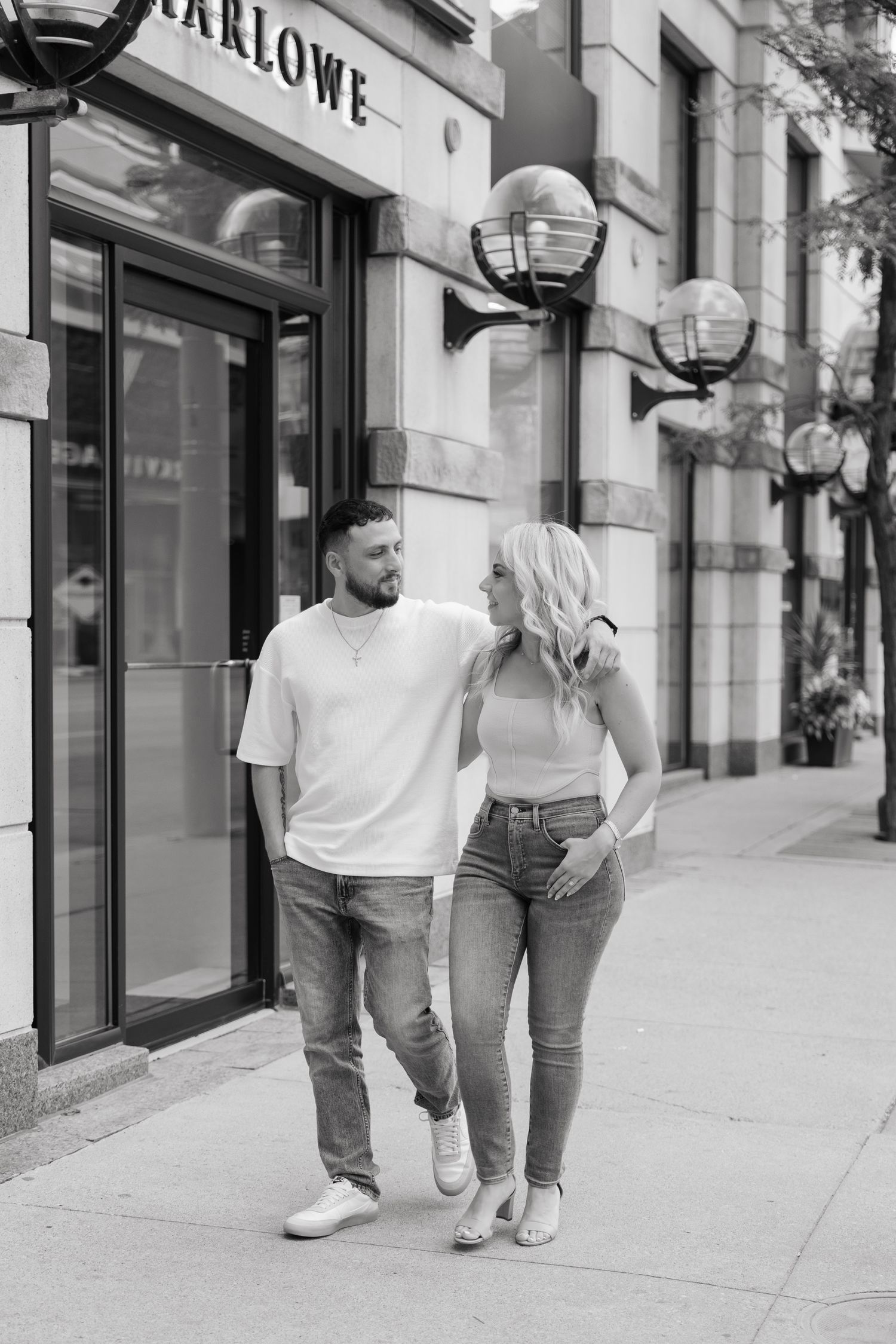 Black and white photo of couple walking together outside retail store.