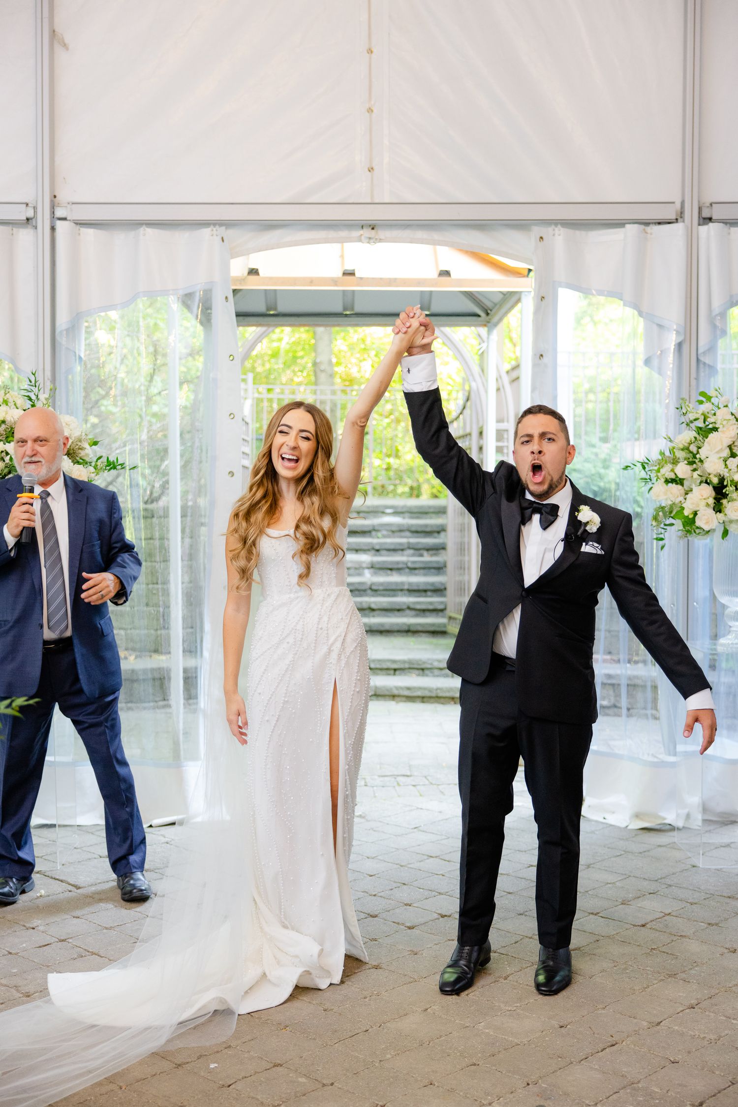 Joyful celebration moment at wedding ceremony with raised hands under white tent.