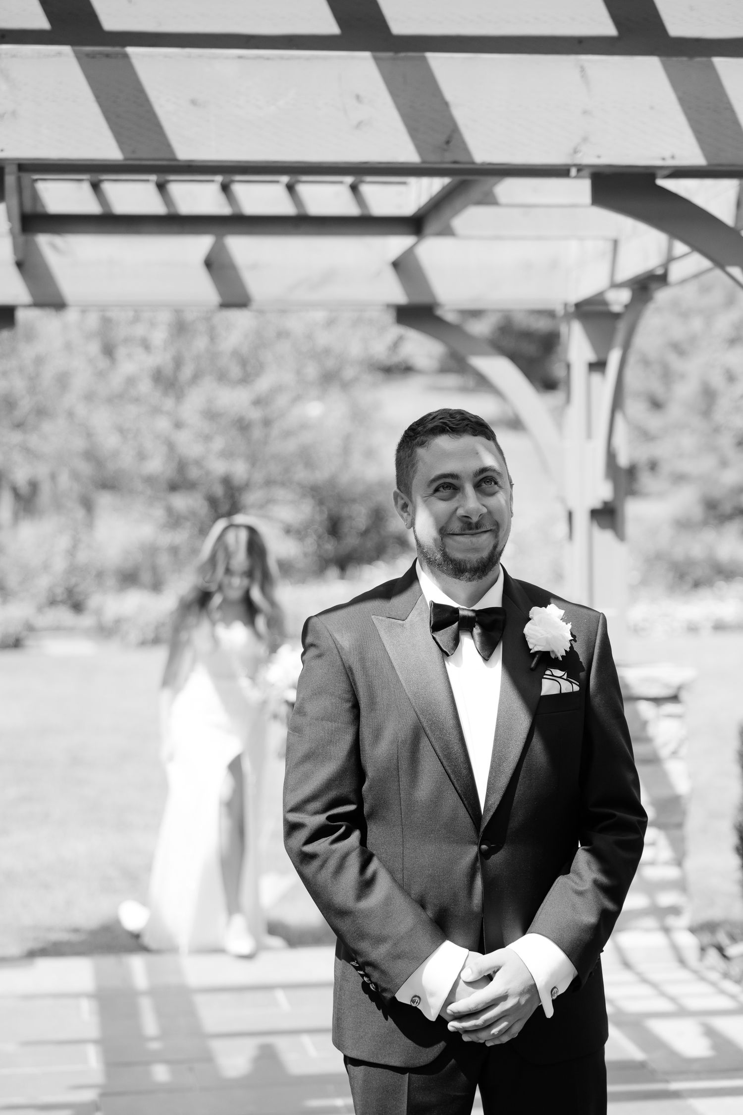 Black and white wedding photo showing a couple during their first look under a pergola.
