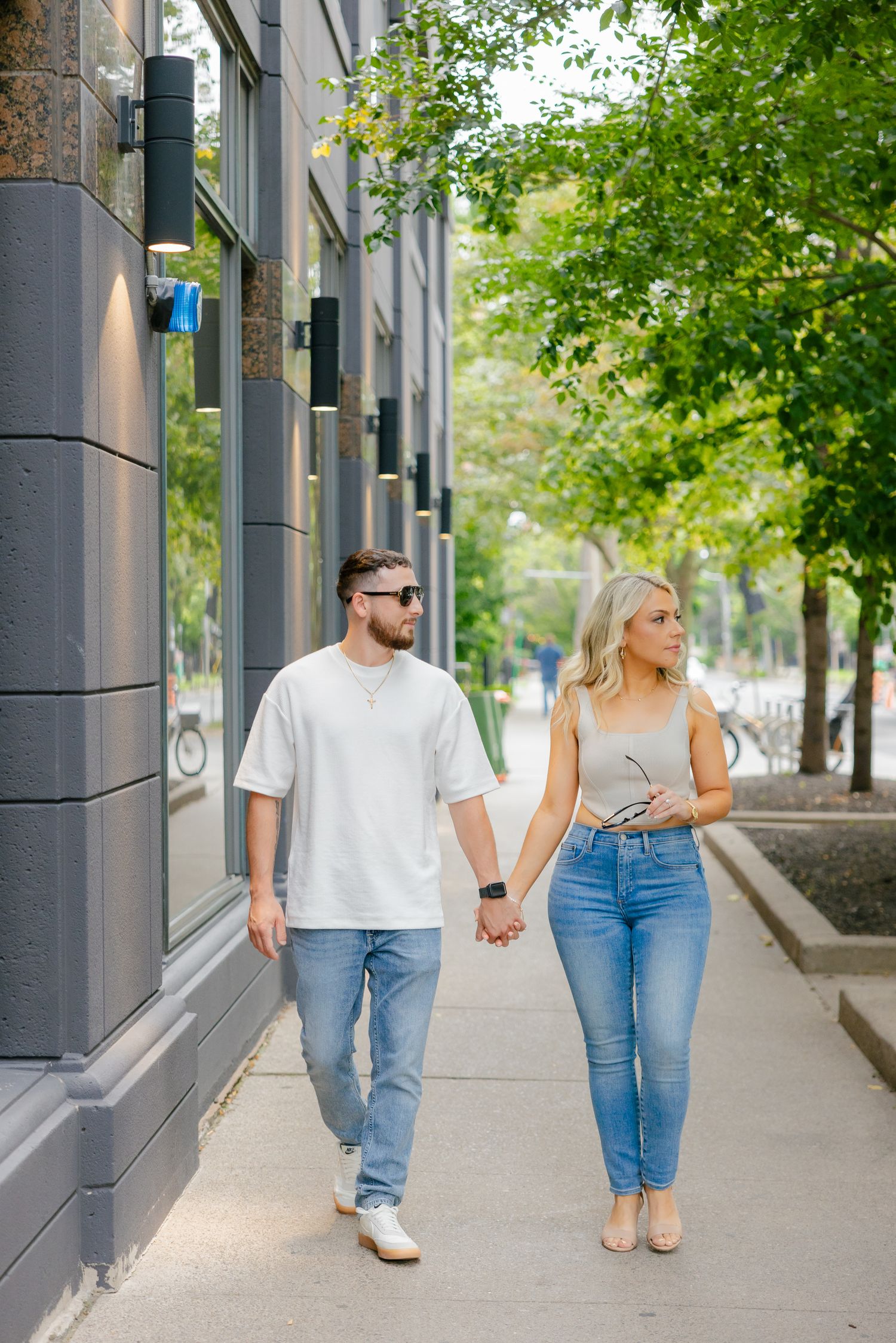 A couple in casual wear holding hands while walking along a city street.