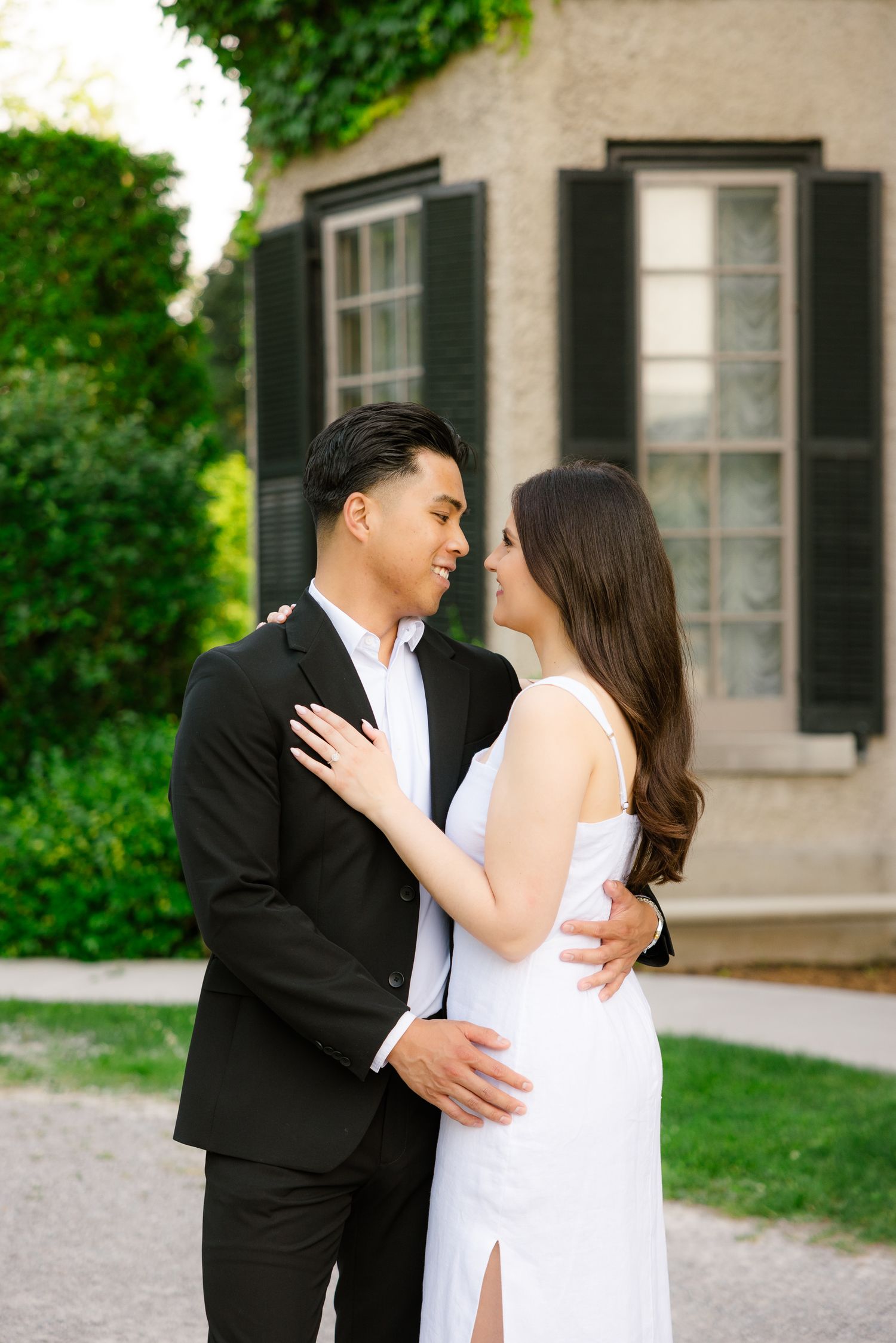 Couple in black and white formal attire sharing intimate moment by mansion window.