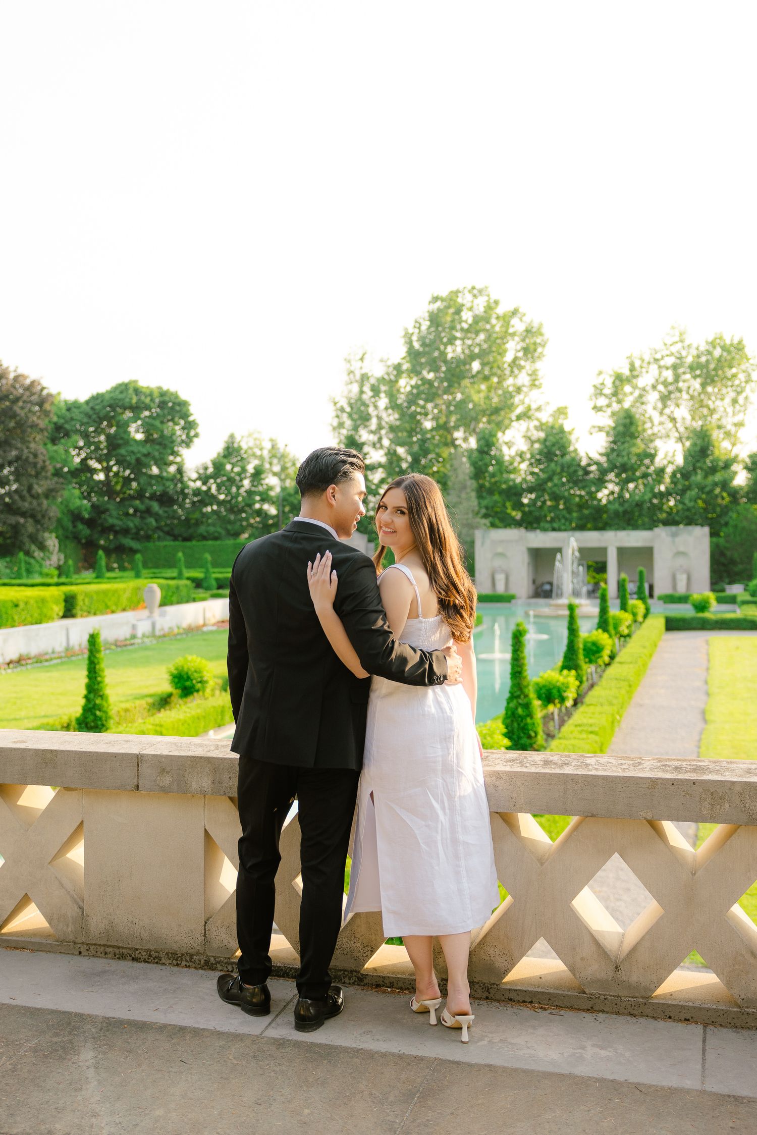 A tender moment shared between a couple on a sunny terrace overlooking formal gardens.