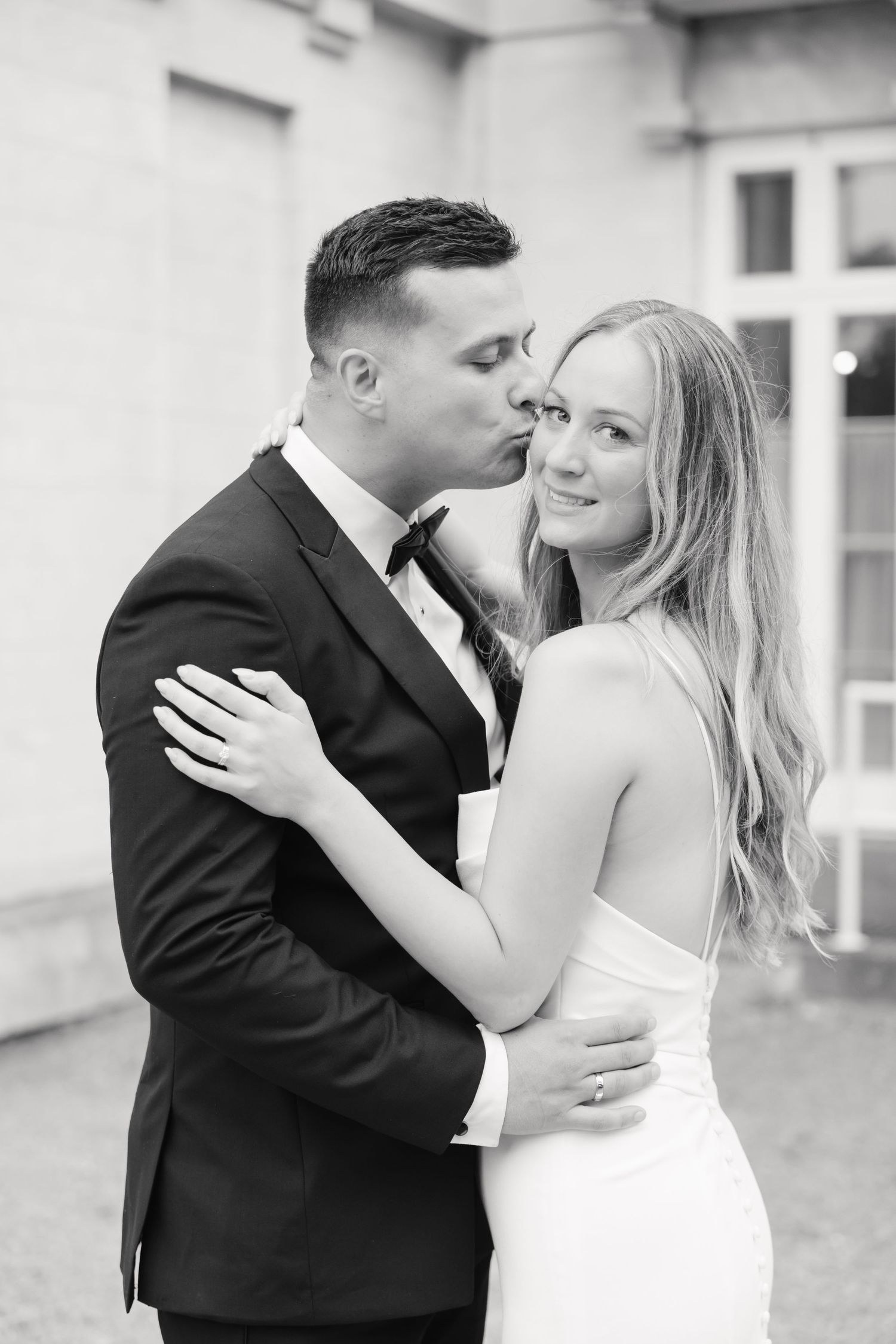 Black and white portrait of newlyweds in an affectionate embrace against light background.