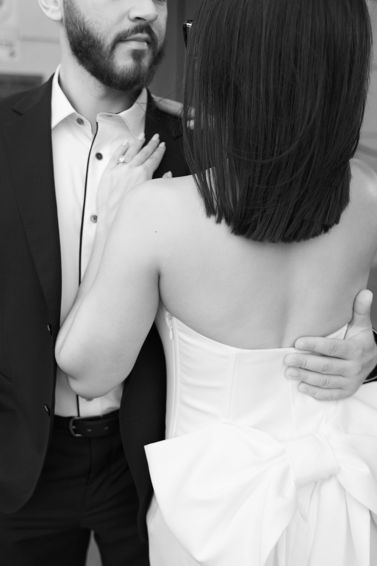 Intimate black and white close-up of a couple embracing, with focus on his suit and her white dress.