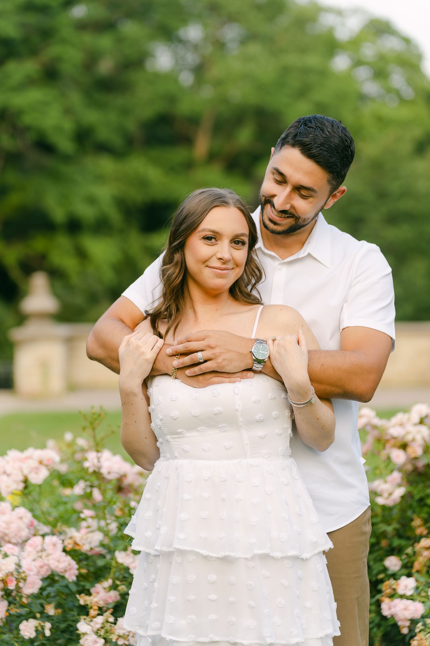A joyful engagement photo featuring a couple embracing among pink rose bushes.