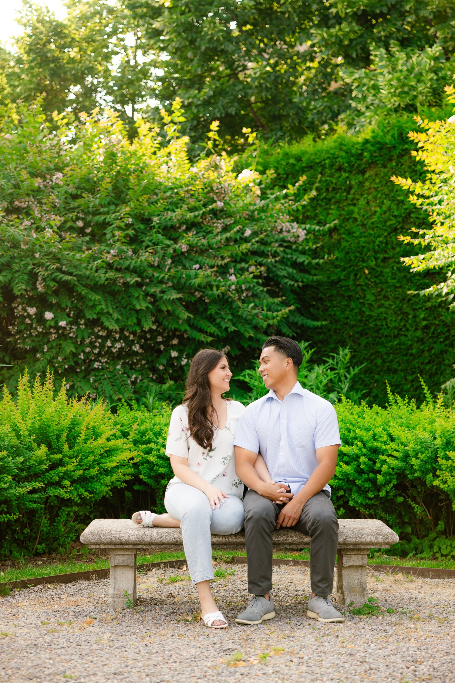 A couple sits together on a stone bench in a lush garden setting during summer.