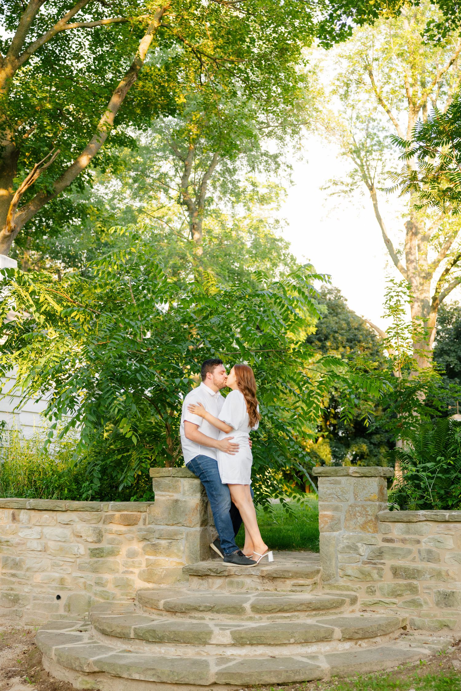 A romantic couple stands together on stone garden steps during golden hour.