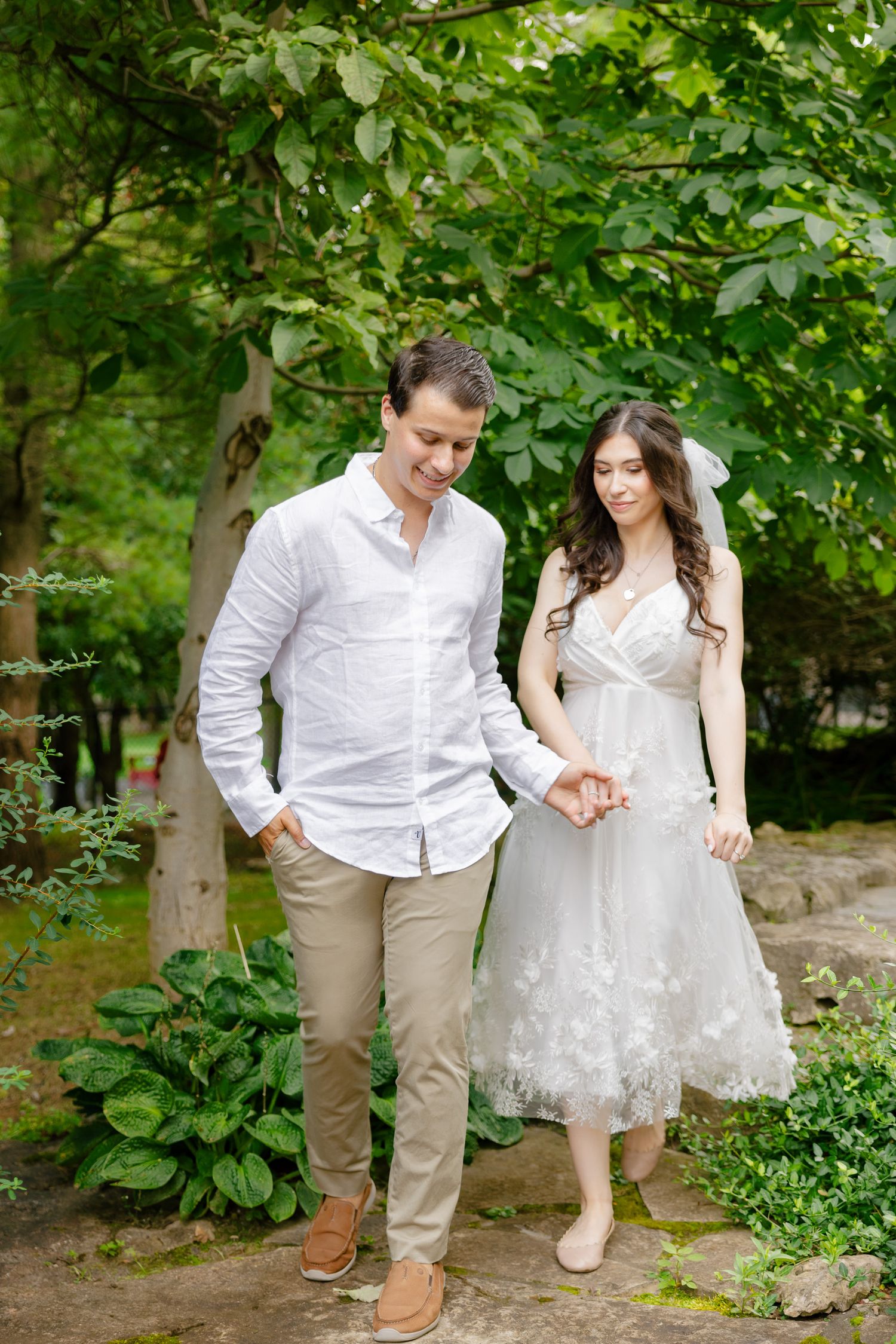 A couple shares a romantic moment in a lush garden setting wearing wedding attire and casual formal wear.