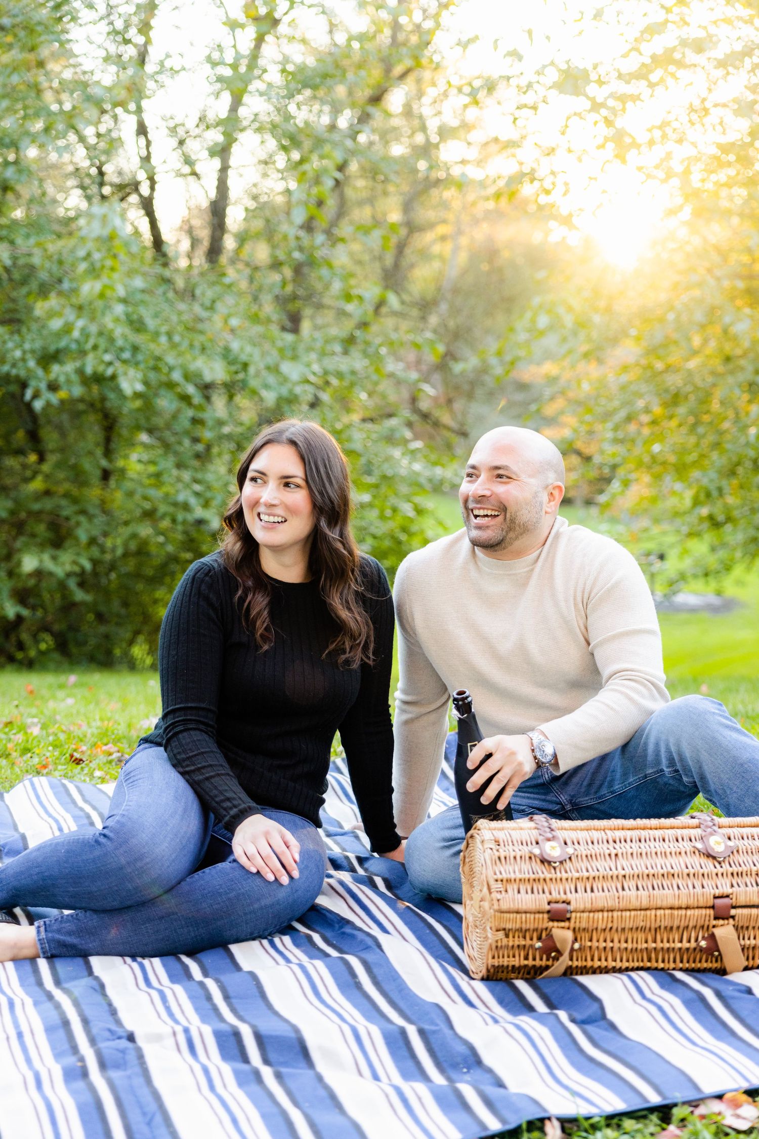 Couple enjoys romantic picnic on striped blanket with wicker basket in sunlit garden setting.
