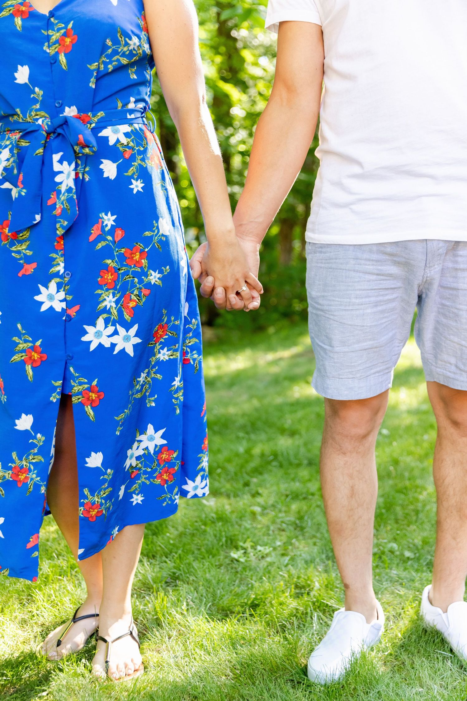 Close-up of couple holding hands, showing blue floral dress and casual summer attire.