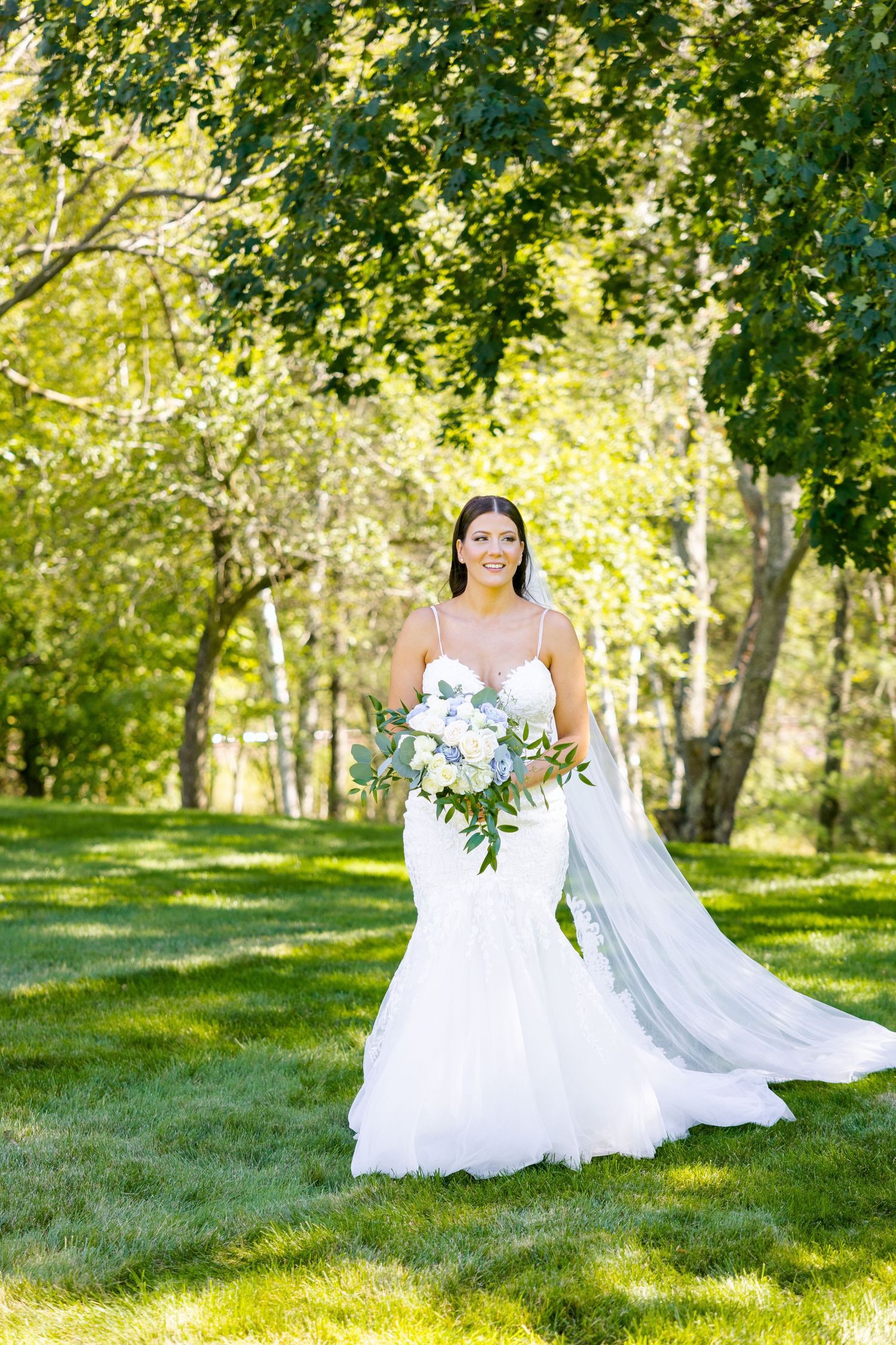 A stunning wedding dress with flowing train photographed in a sun-dappled garden.