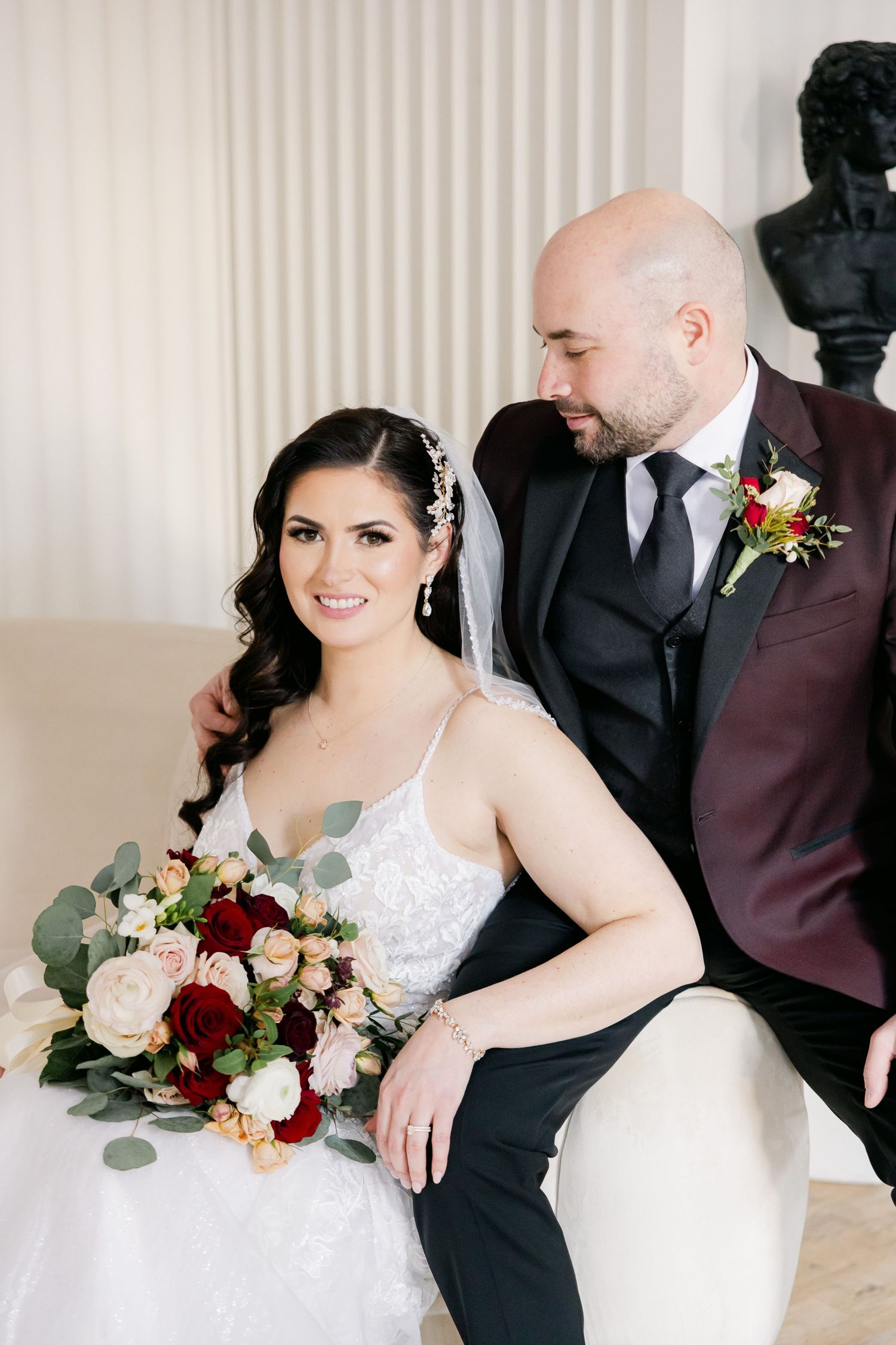 Elegant wedding portrait featuring couple in burgundy and white with lush floral bouquet.