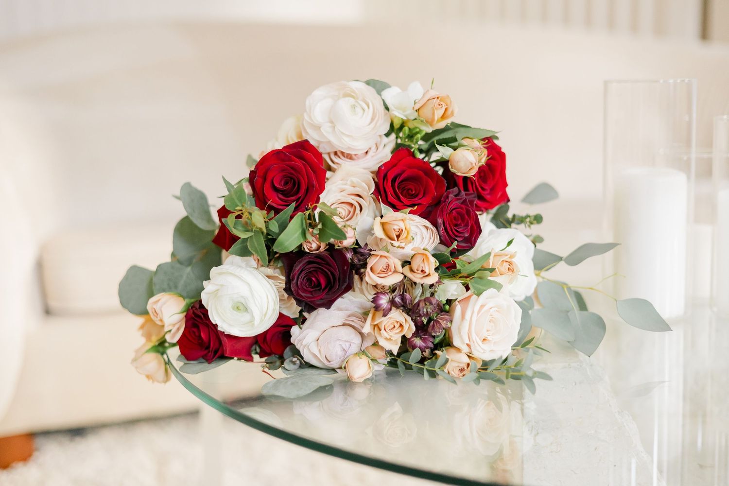 Luxurious bridal bouquet featuring red and white roses with eucalyptus on glass table.