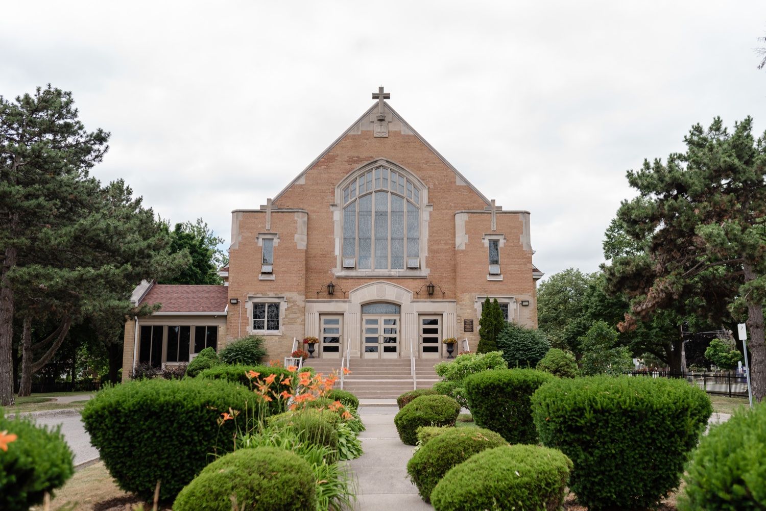 Exterior view of traditional brick church with arched windows and manicured garden landscape.