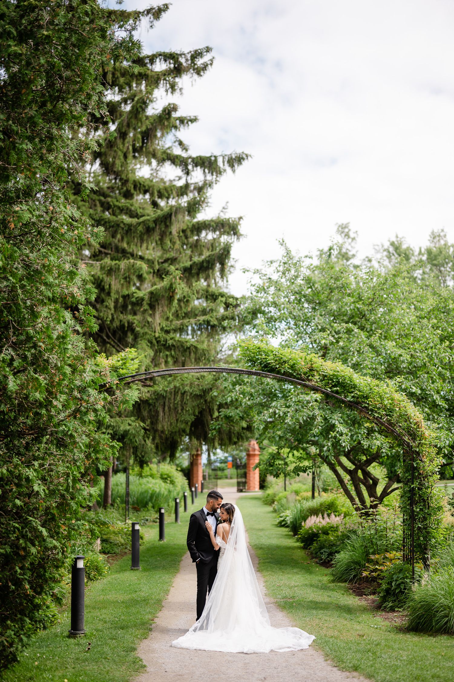 Newlyweds pose under a lush garden arch on their wedding day.