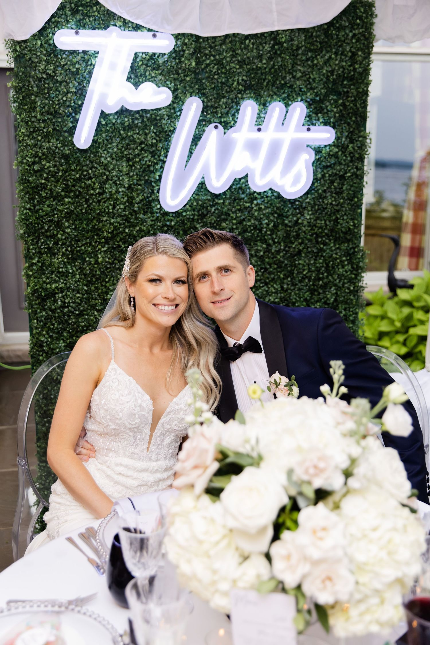 Wedding photo backdrop featuring green hedge wall with white neon signage and floral decorations.