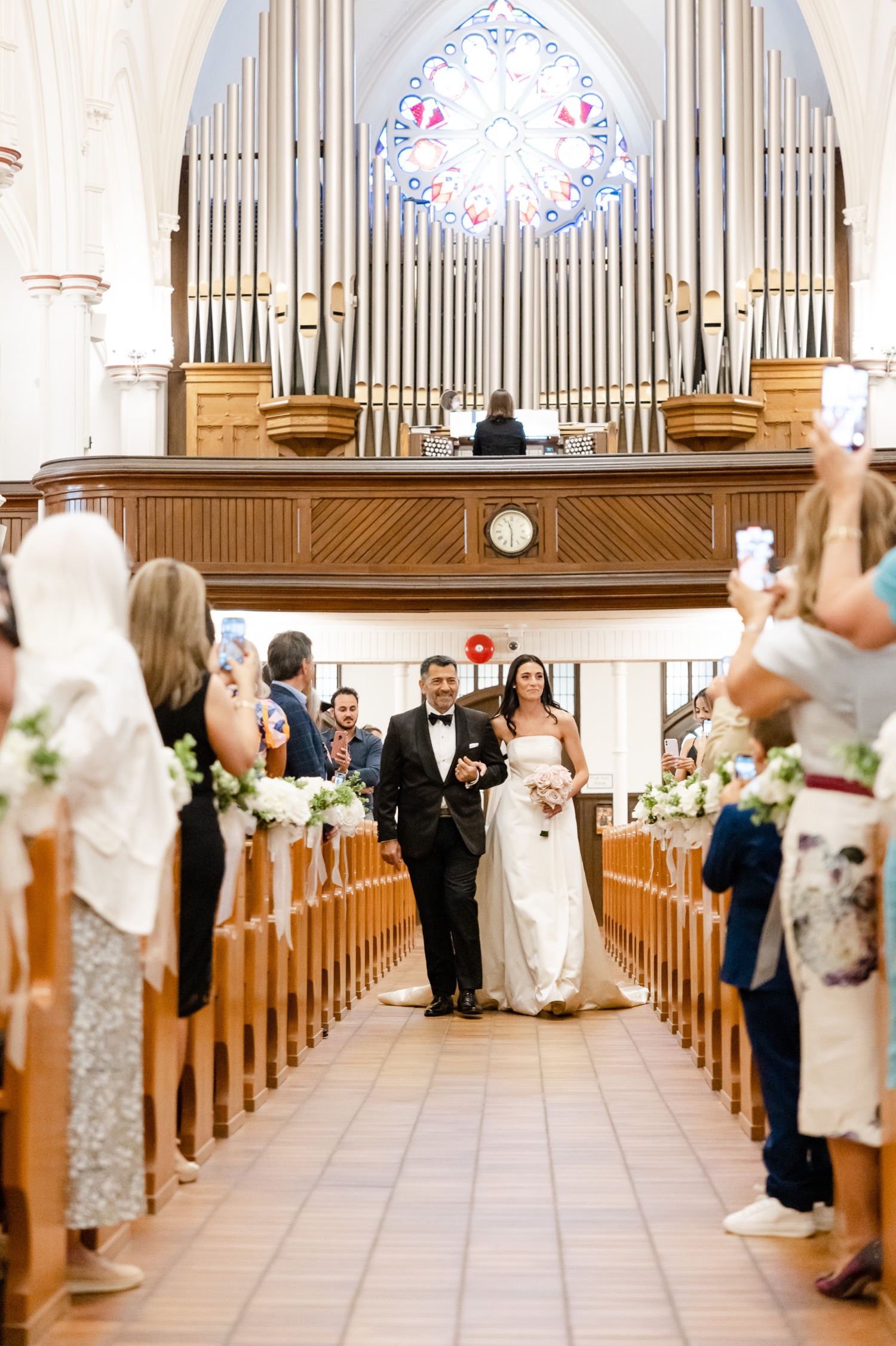 Wedding ceremony in traditional church with pipe organ and guests lining wooden pews.