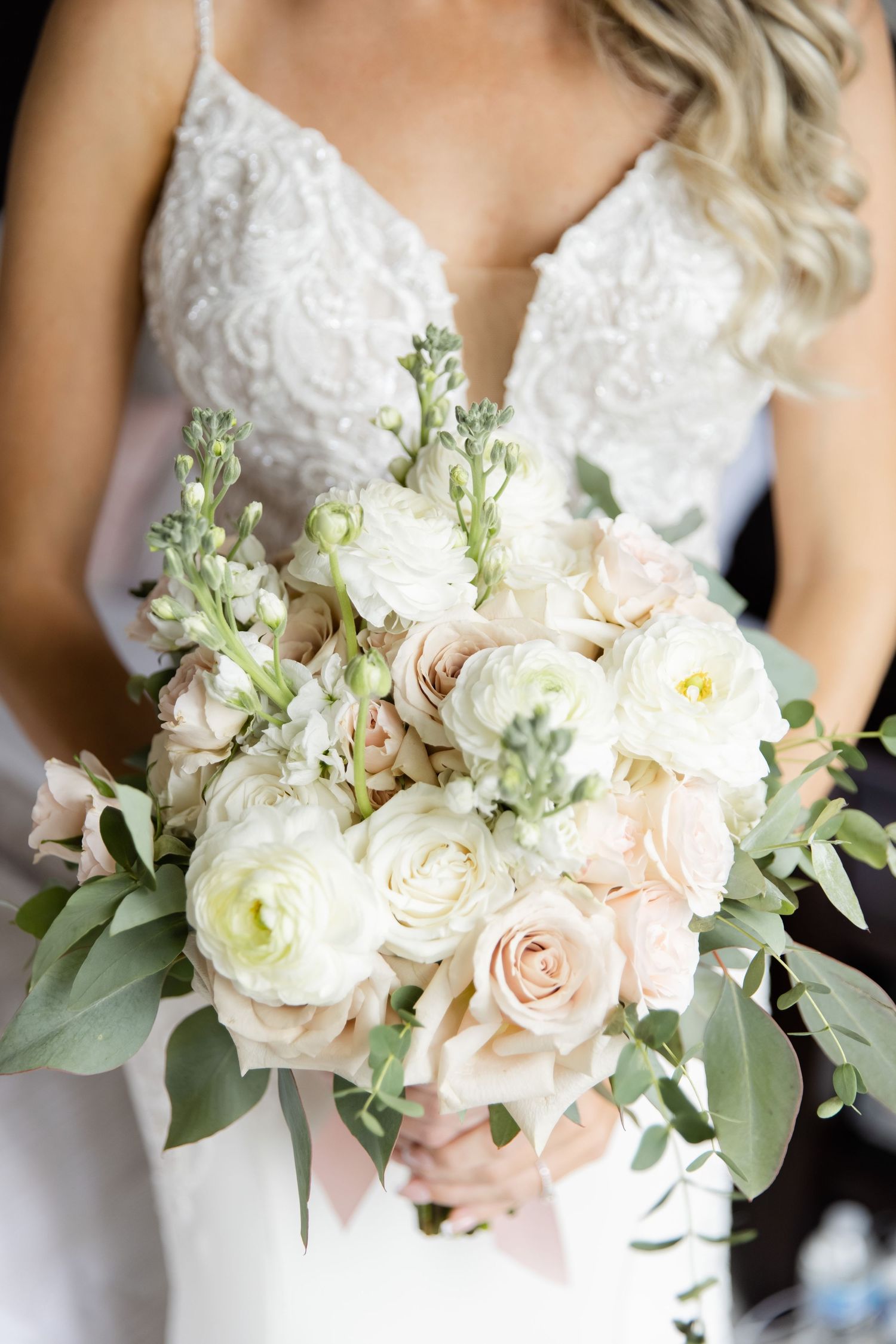 Delicate bridal bouquet with white and blush roses, ranunculus, and greenery against a lace wedding dress.