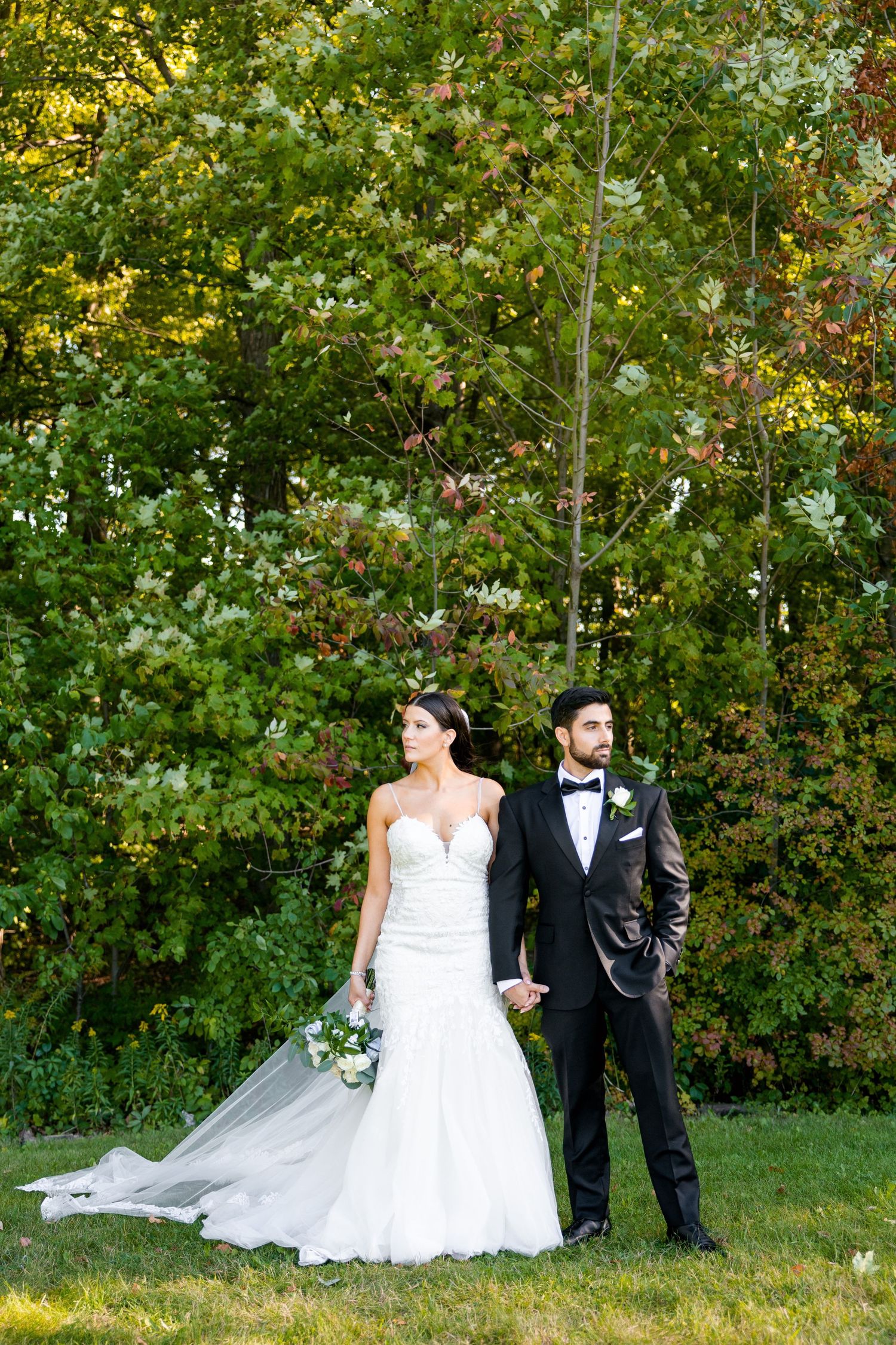 A elegant wedding portrait featuring a couple in formal attire against a backdrop of autumn trees.
