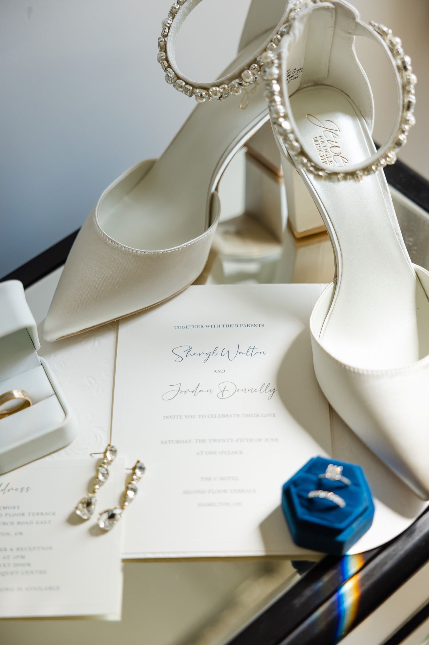 Crisp white wedding shoes with rhinestone straps arranged with invitation and ring box.
