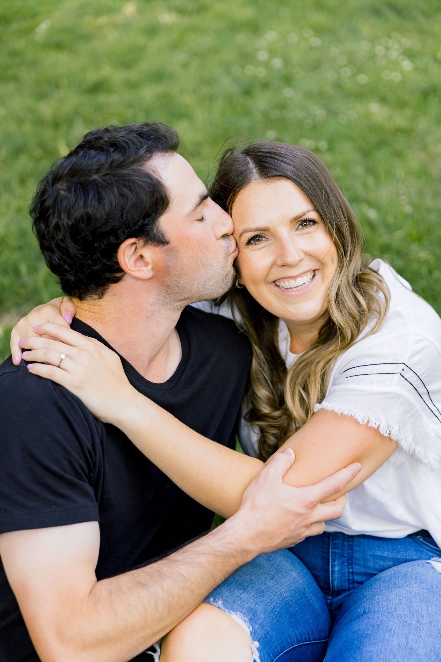 A romantic couple shares tender moments while sitting together outdoors on a sunny day.