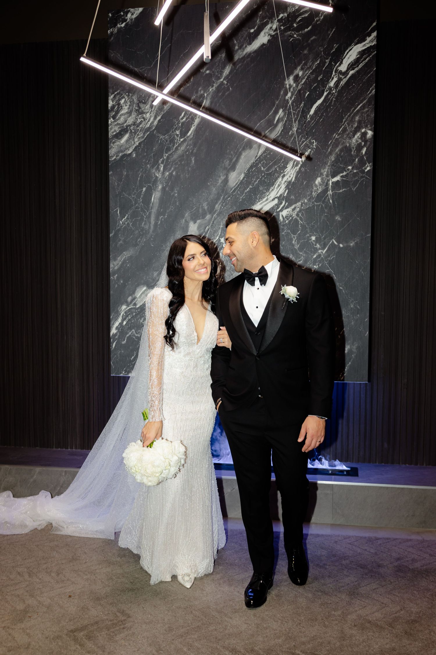 Elegant couple shares a romantic moment against a marble wall backdrop at their wedding celebration.