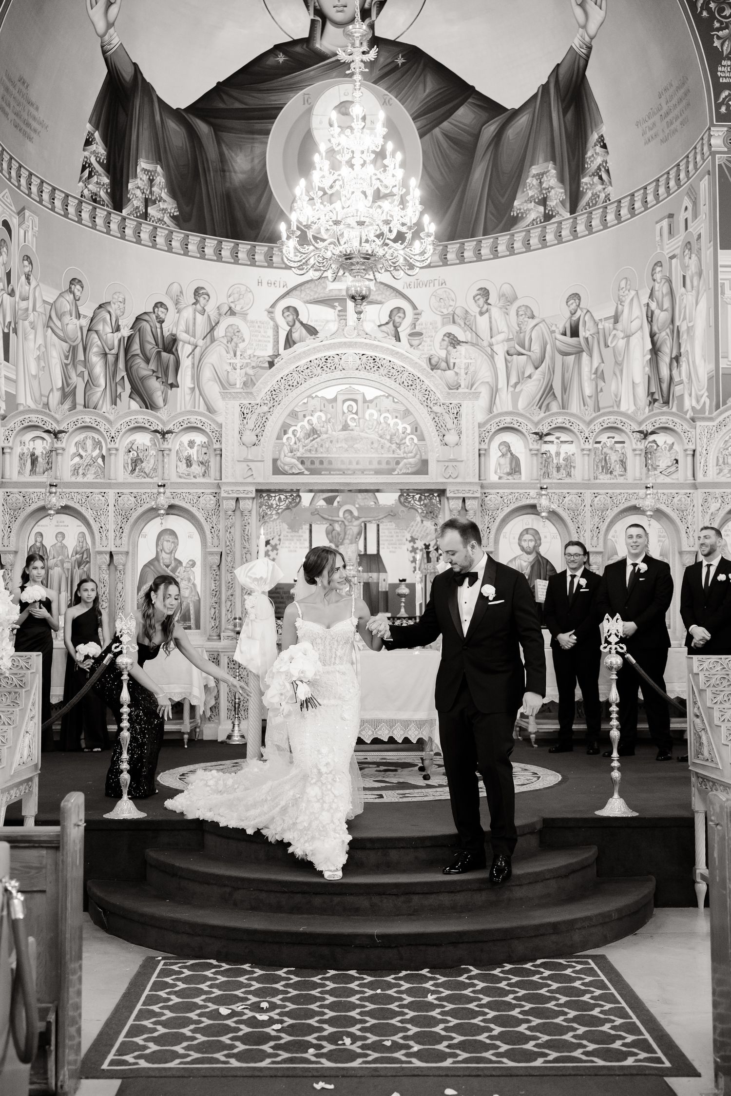 Elegant wedding ceremony in an ornate church with decorative murals and chandeliers as the couple stands at the altar.