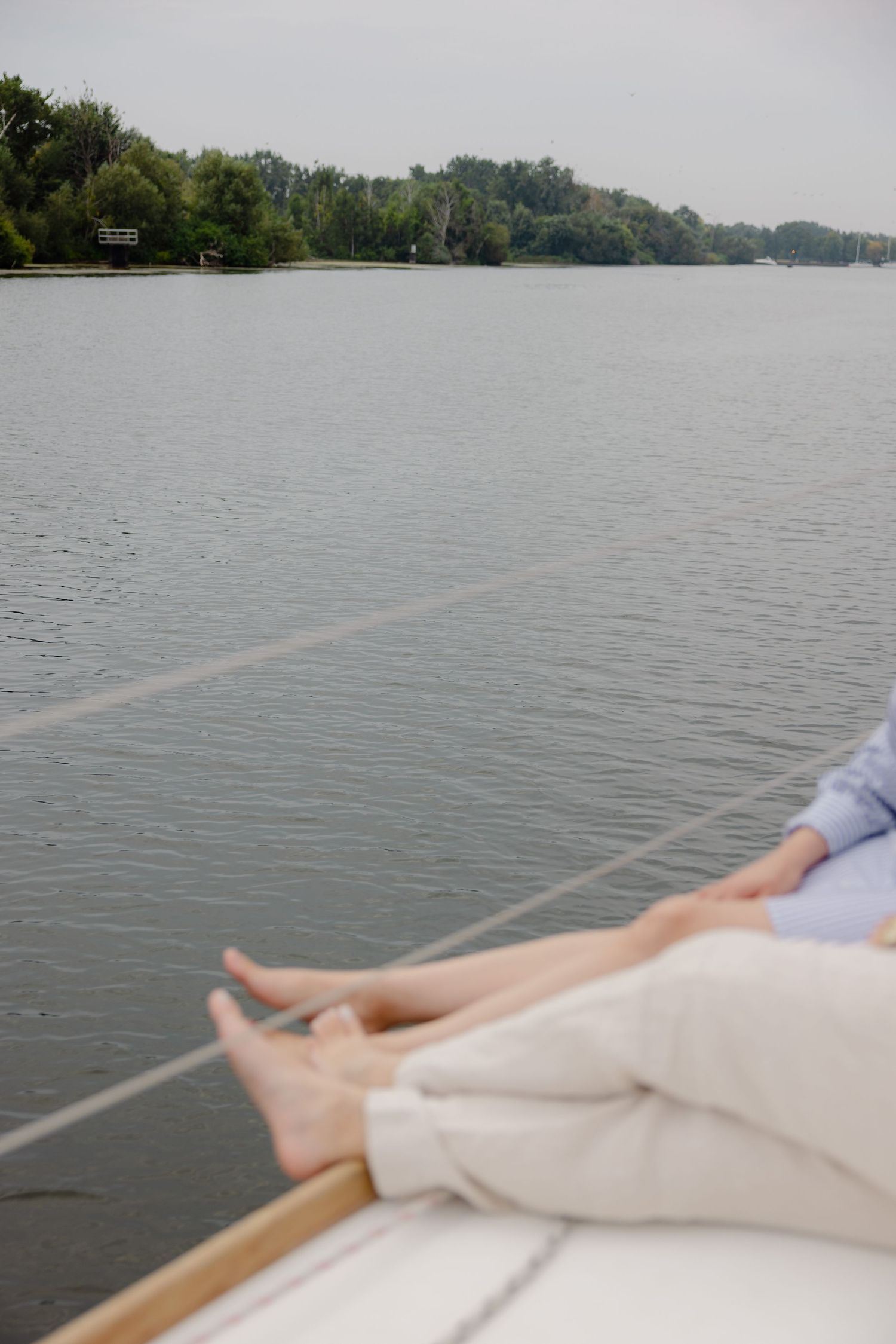 View of relaxed legs resting on a boat deck overlooking a tranquil lake with wooded shoreline in the distance.