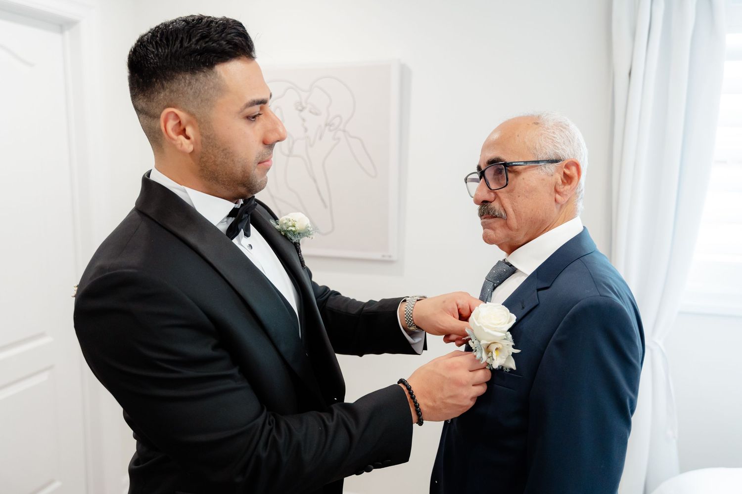 An intimate moment of boutonniere pinning between two formally dressed men.
