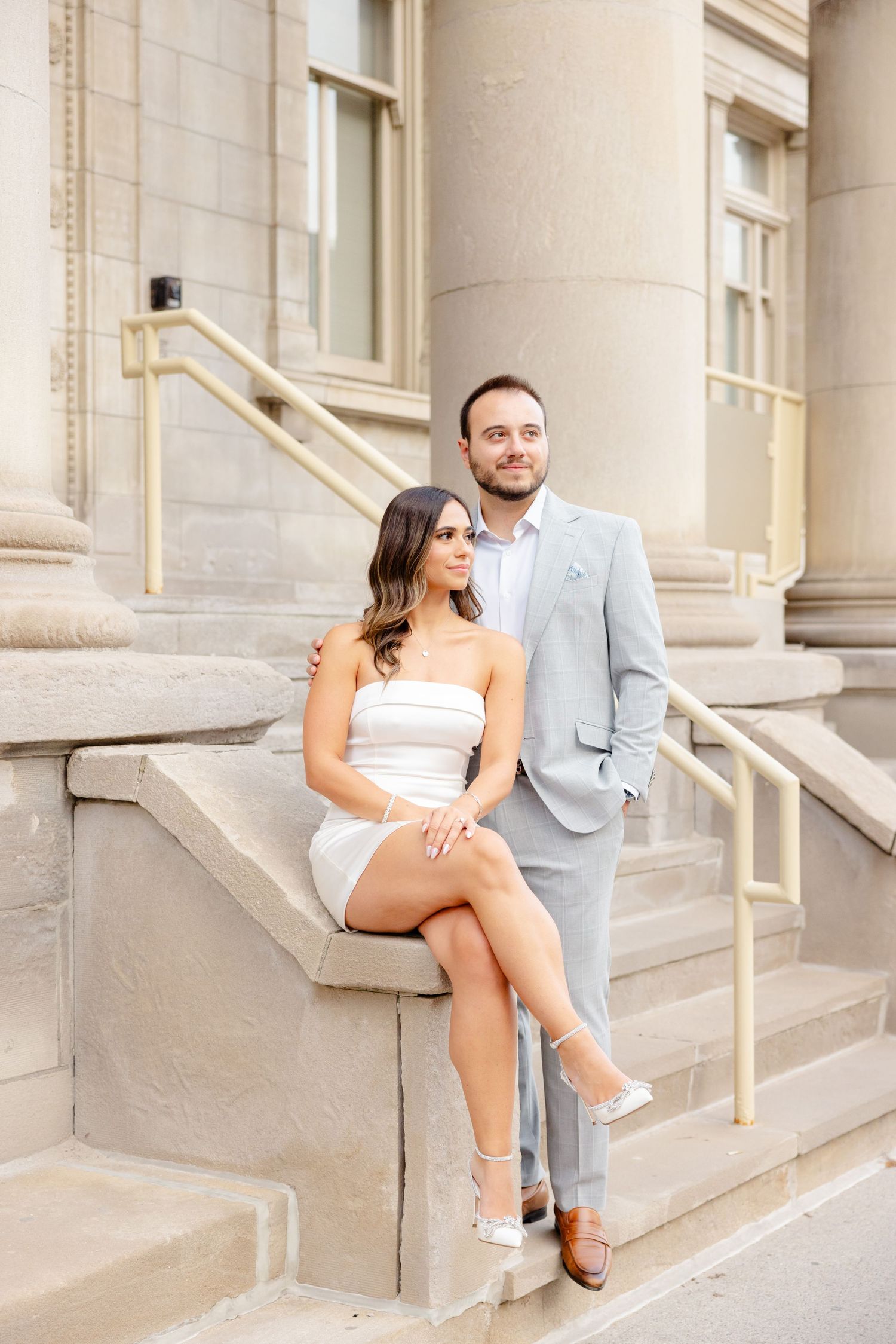A couple in formal attire poses on stone steps against a classic columned building.