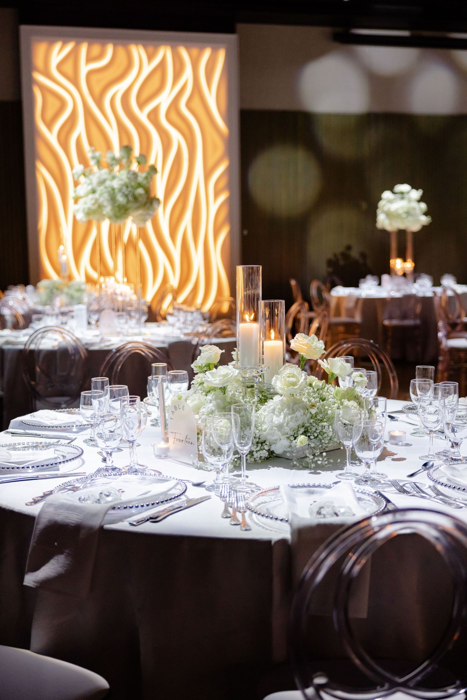 Wedding reception table with dramatic orange backlit wall panel and white floral arrangements.