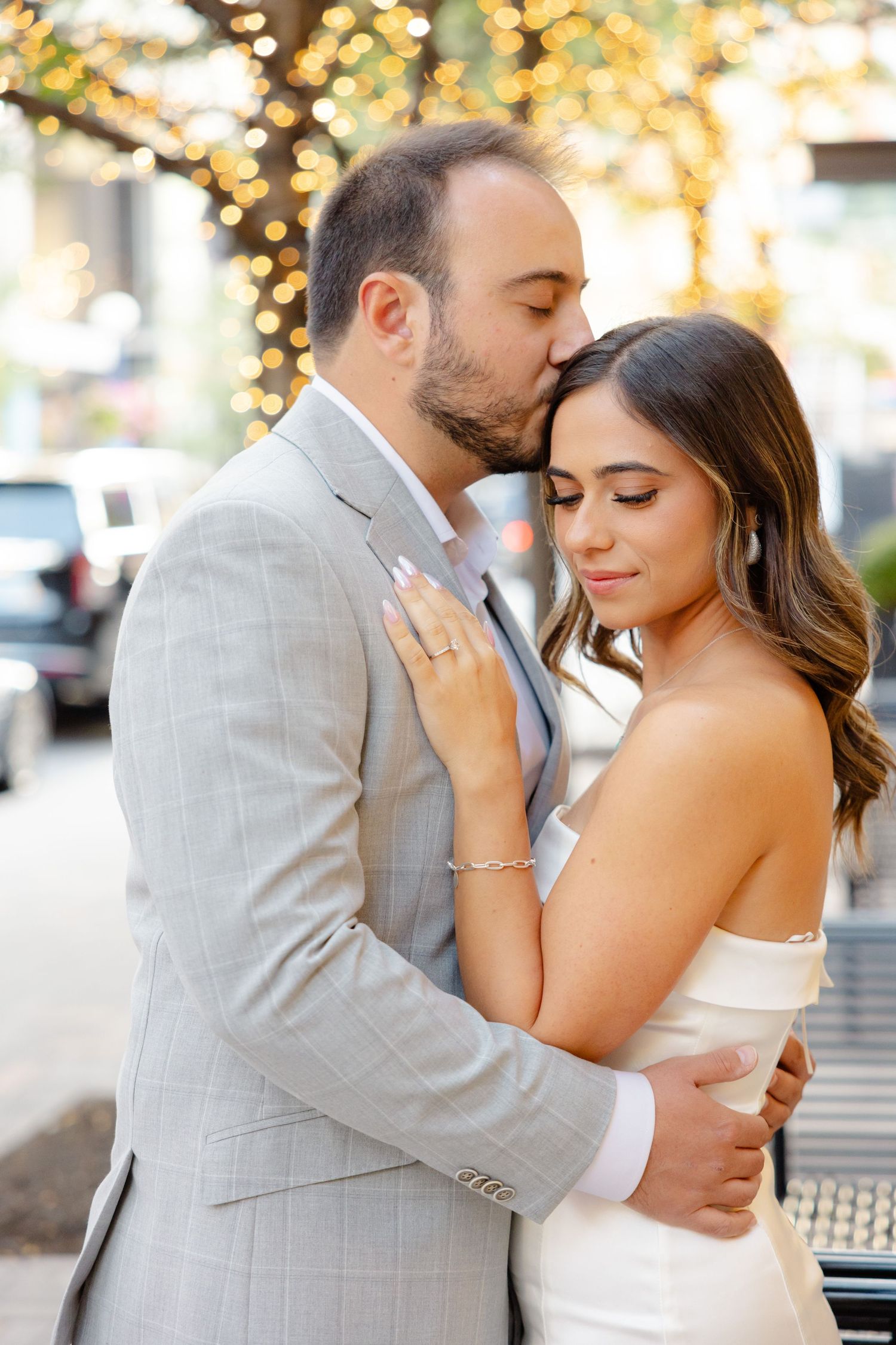 Intimate moment between couple in formal wear with string lights glowing behind them.