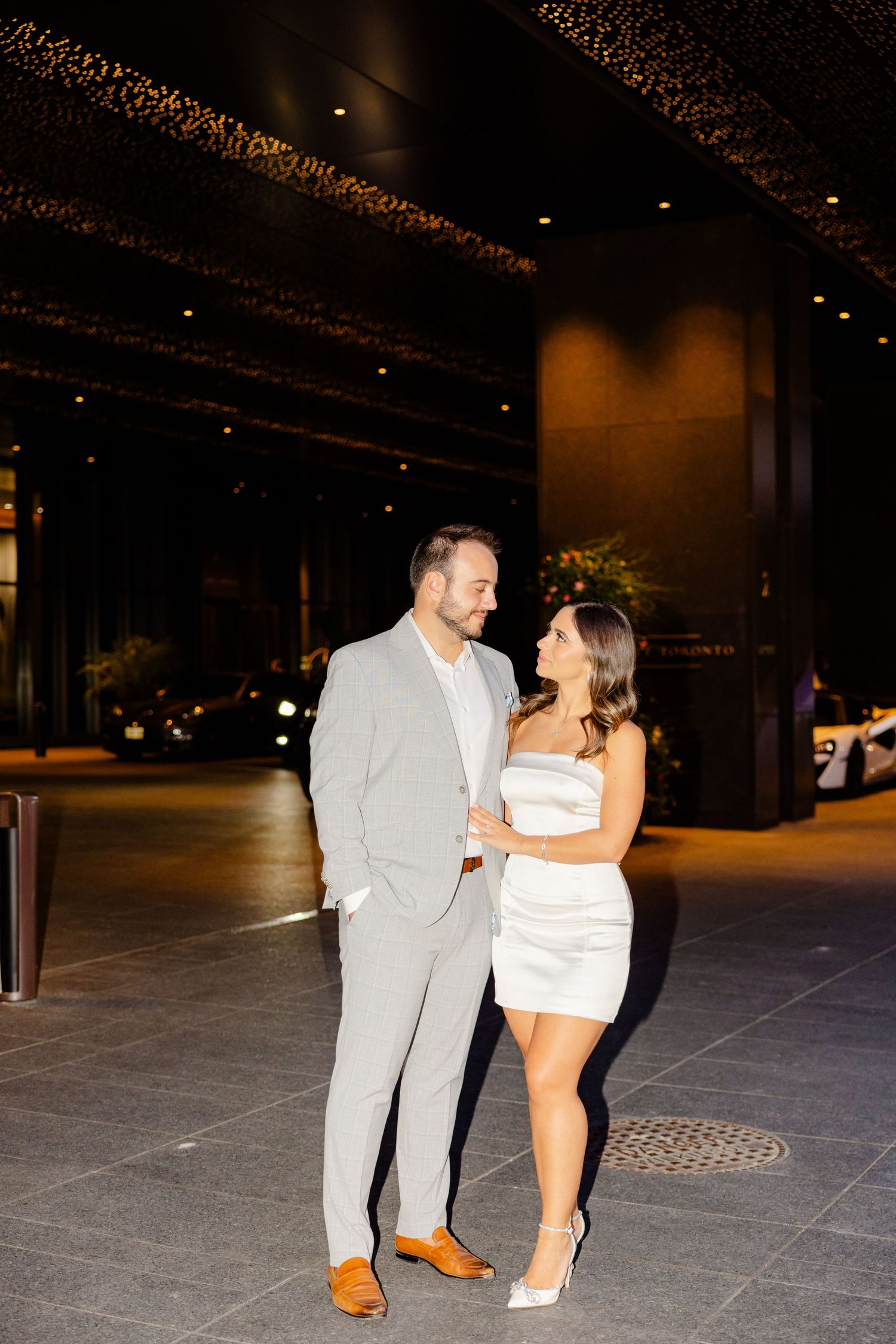 Stylish couple embraces on city plaza with illuminated ceiling above.