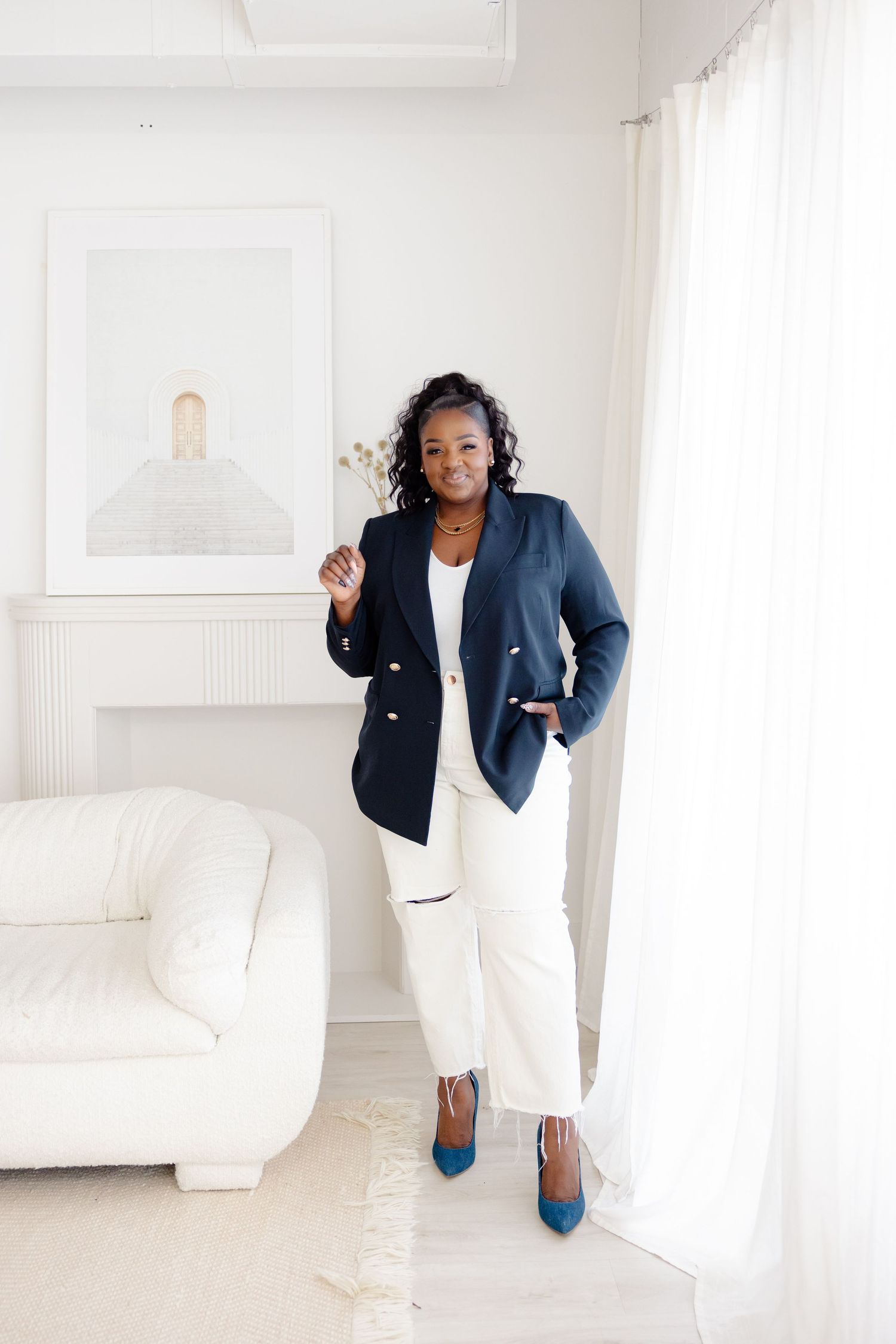 Professional styling in a bright white room featuring navy blazer, white trousers and blue heels against minimalist decor.