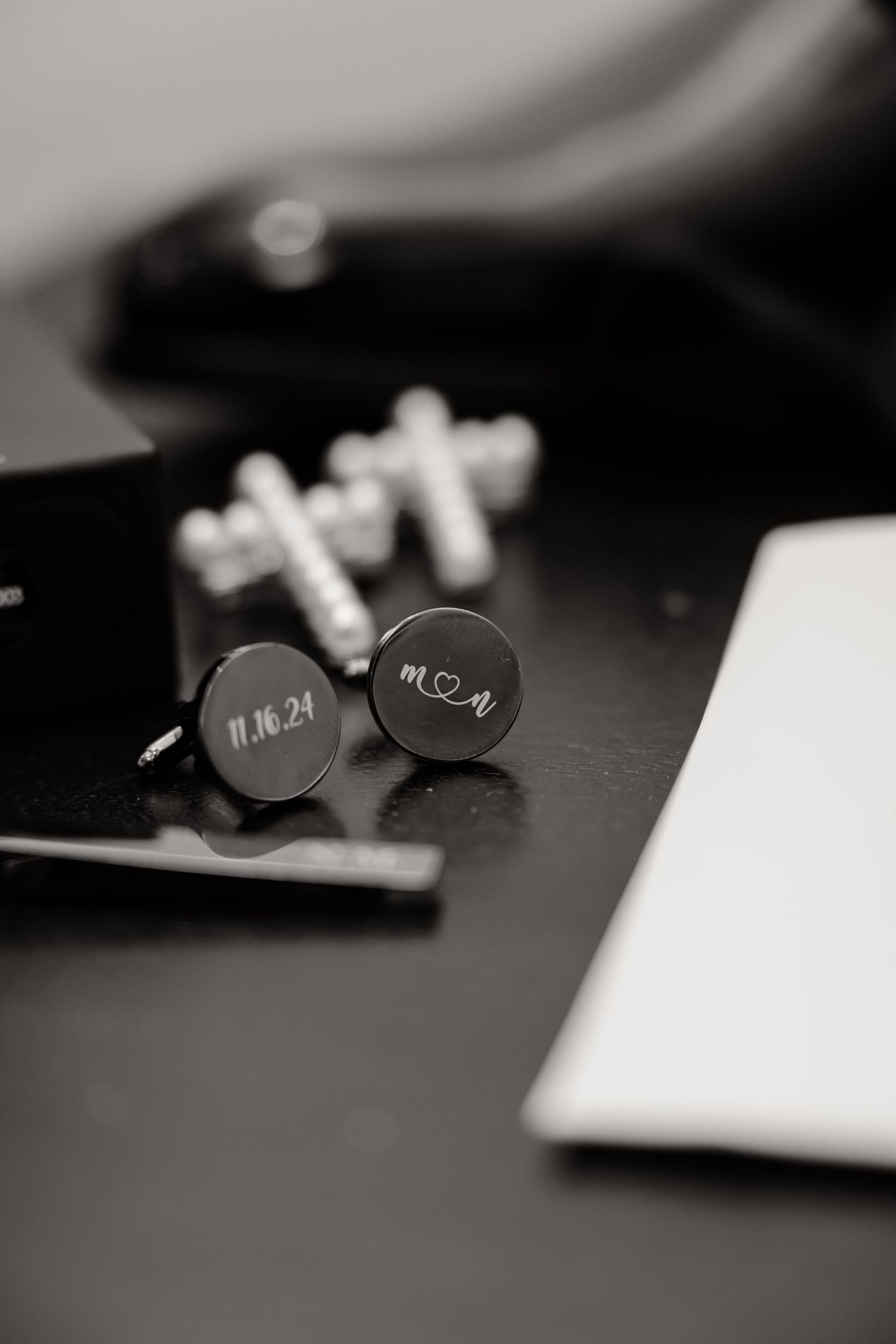 Close-up of engraved cufflinks with wedding date on dark surface.
