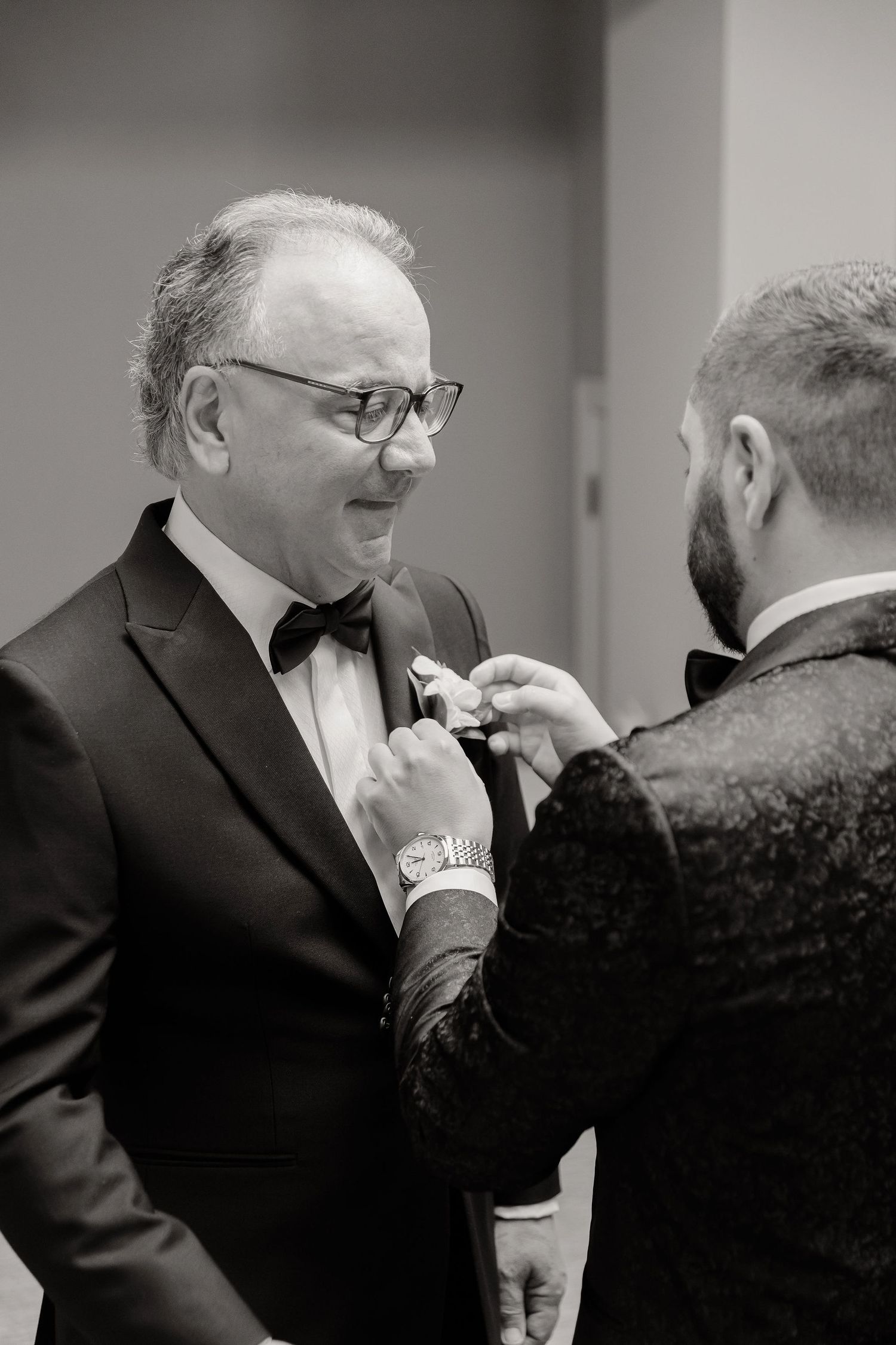 Black and white sequence of someone helping another adjust their bow tie before a formal occasion.