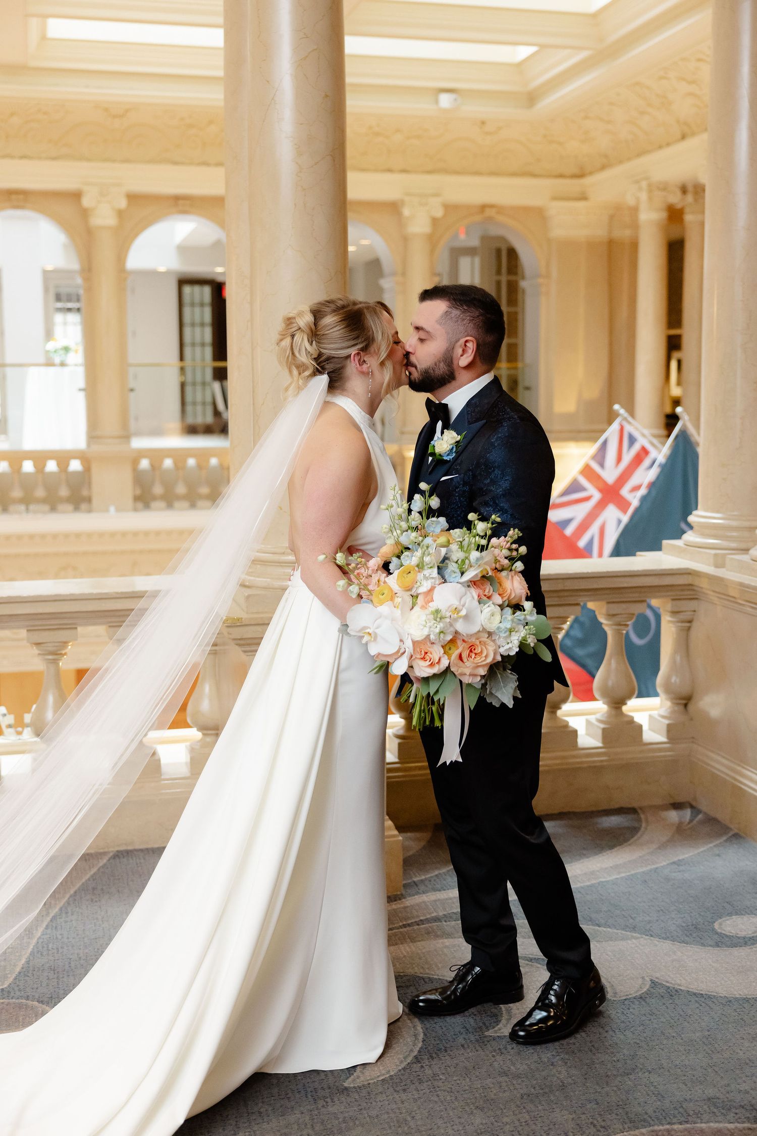 Elegant wedding couple sharing intimate moment in grand hallway with British flags and architectural details.