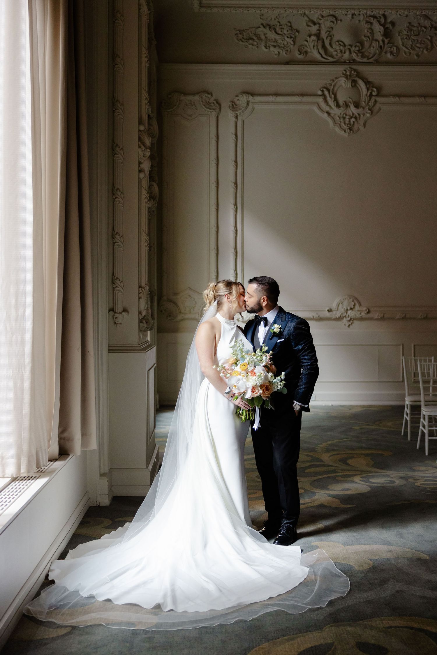 Elegant wedding couple photographed in ornate room with decorative moldings and long train.