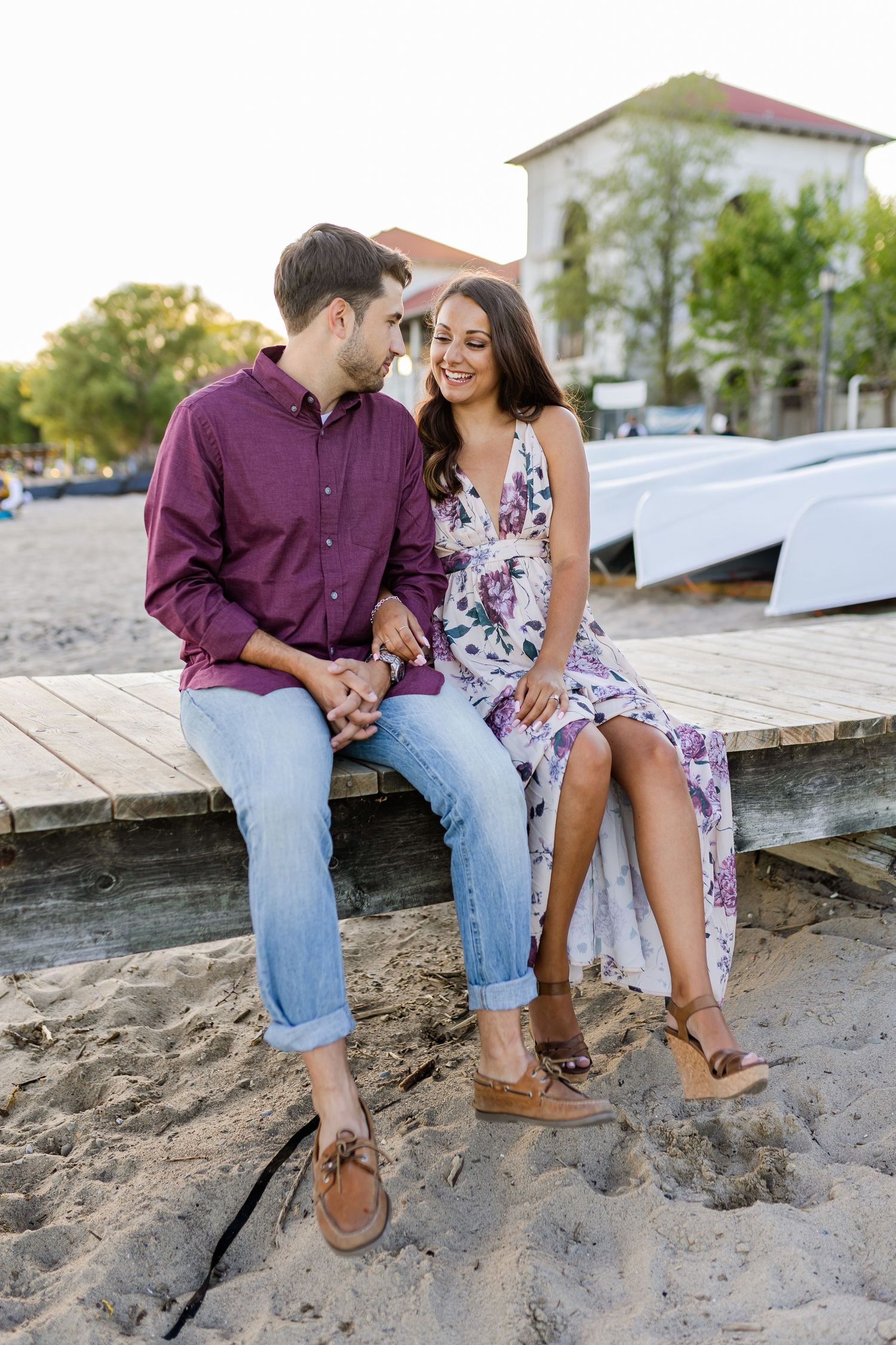 Romantic waterfront scene with couple sitting on wooden dock near white boats.