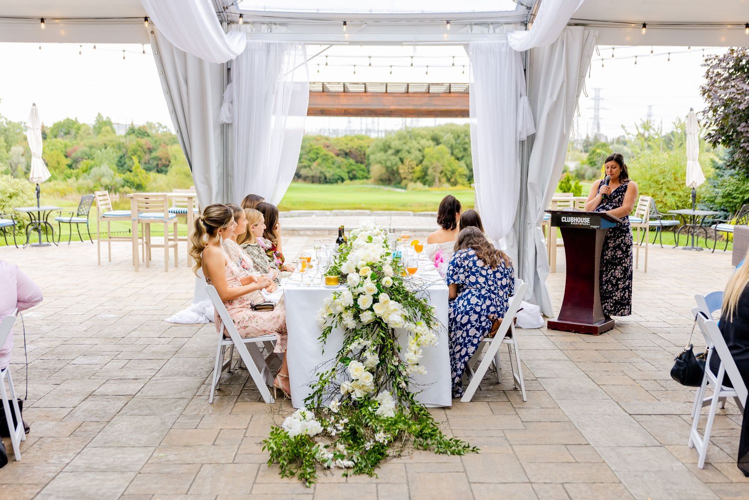 Elegant outdoor reception setup with white draping and floral centerpieces.