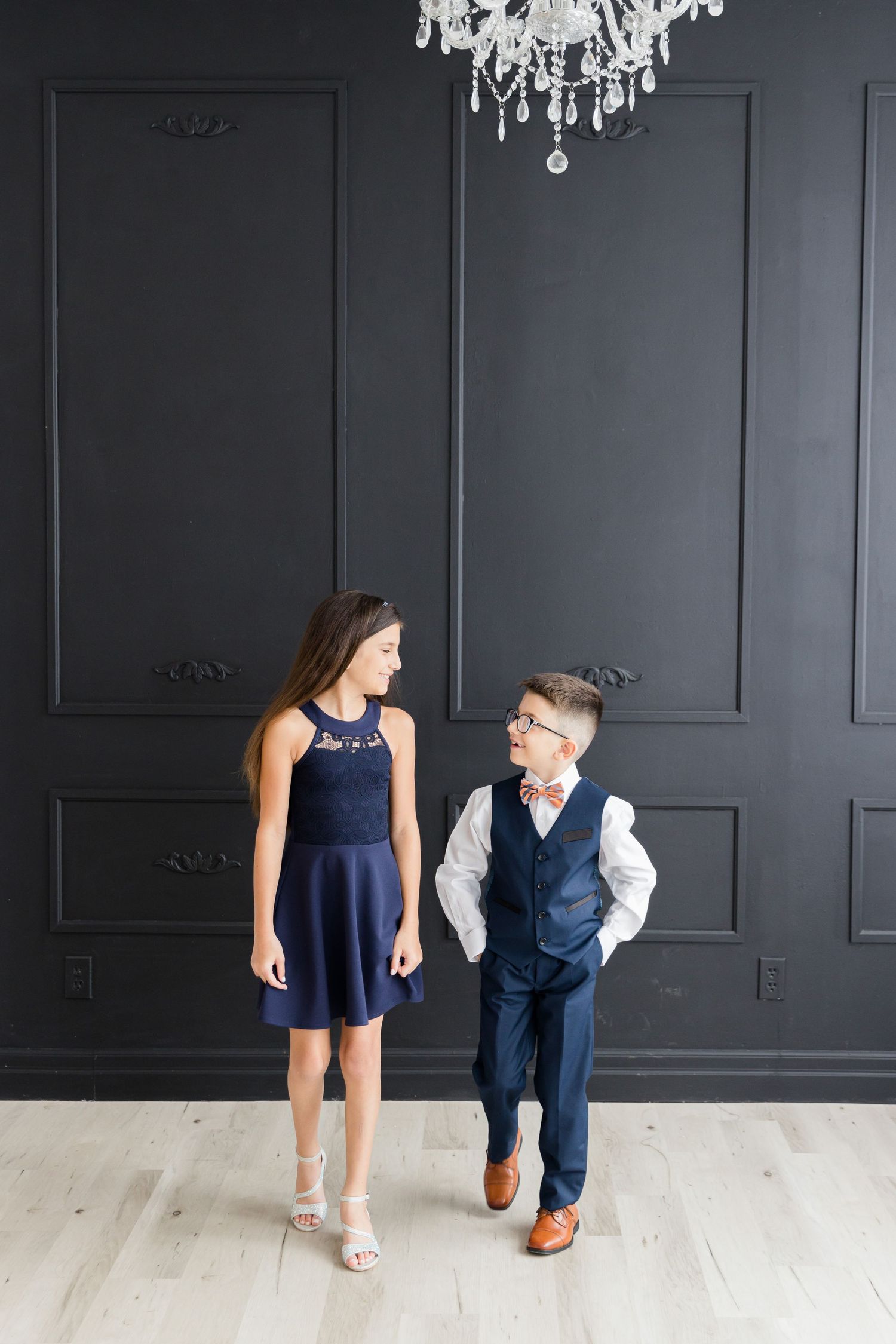 Elegant formal photo under crystal chandelier against dark paneled wall wearing navy attire.
