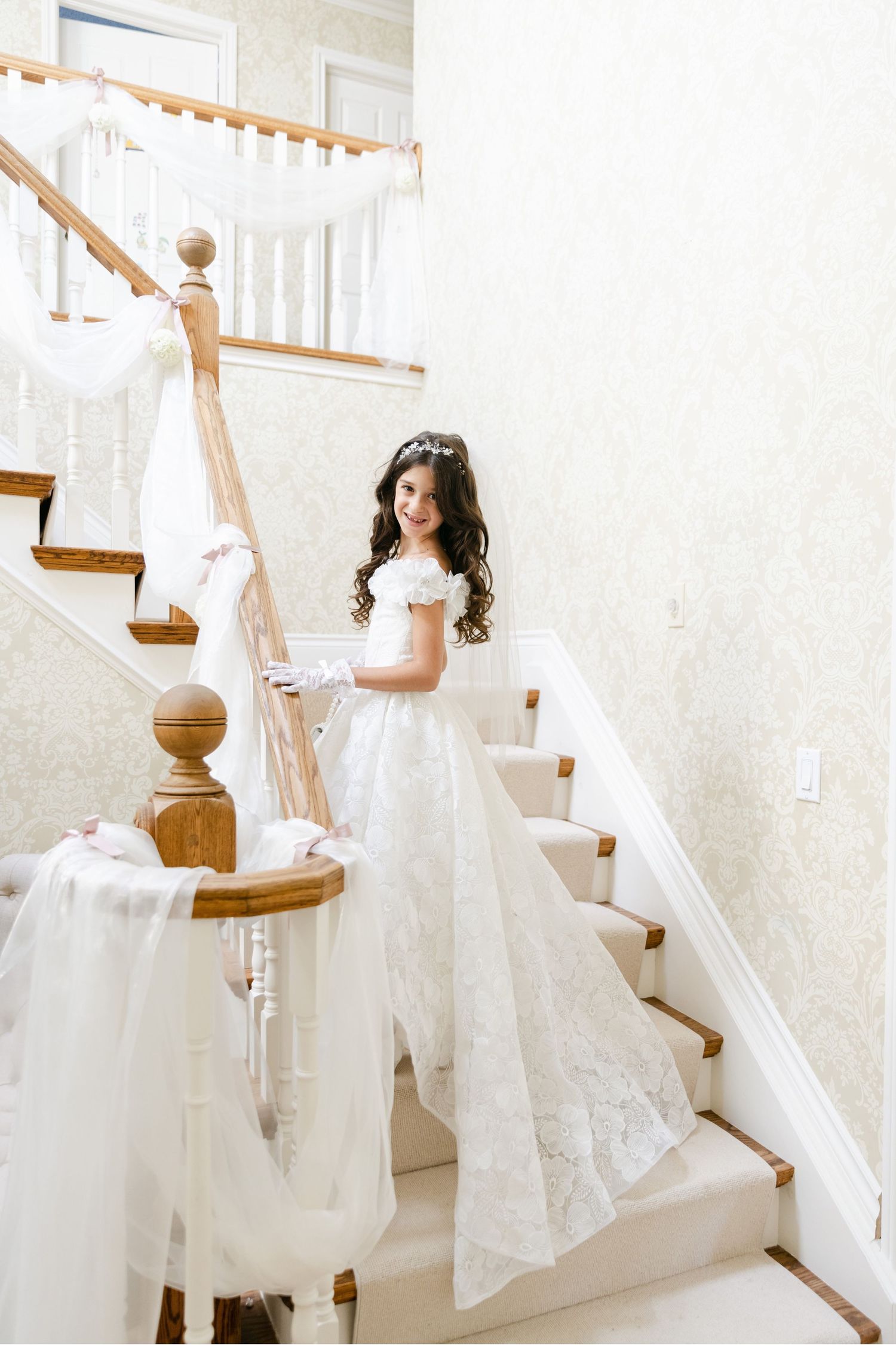 Elegant white baptismal gown with lace details photographed on carpeted staircase.
